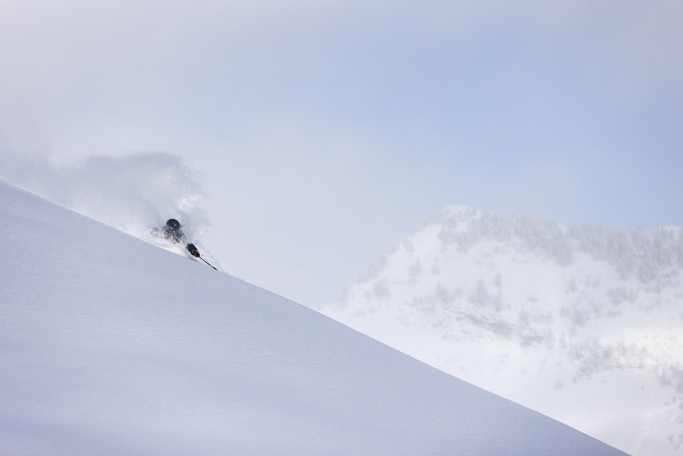 Skier Drew Gilmore skis through deep snow with mountains in the background