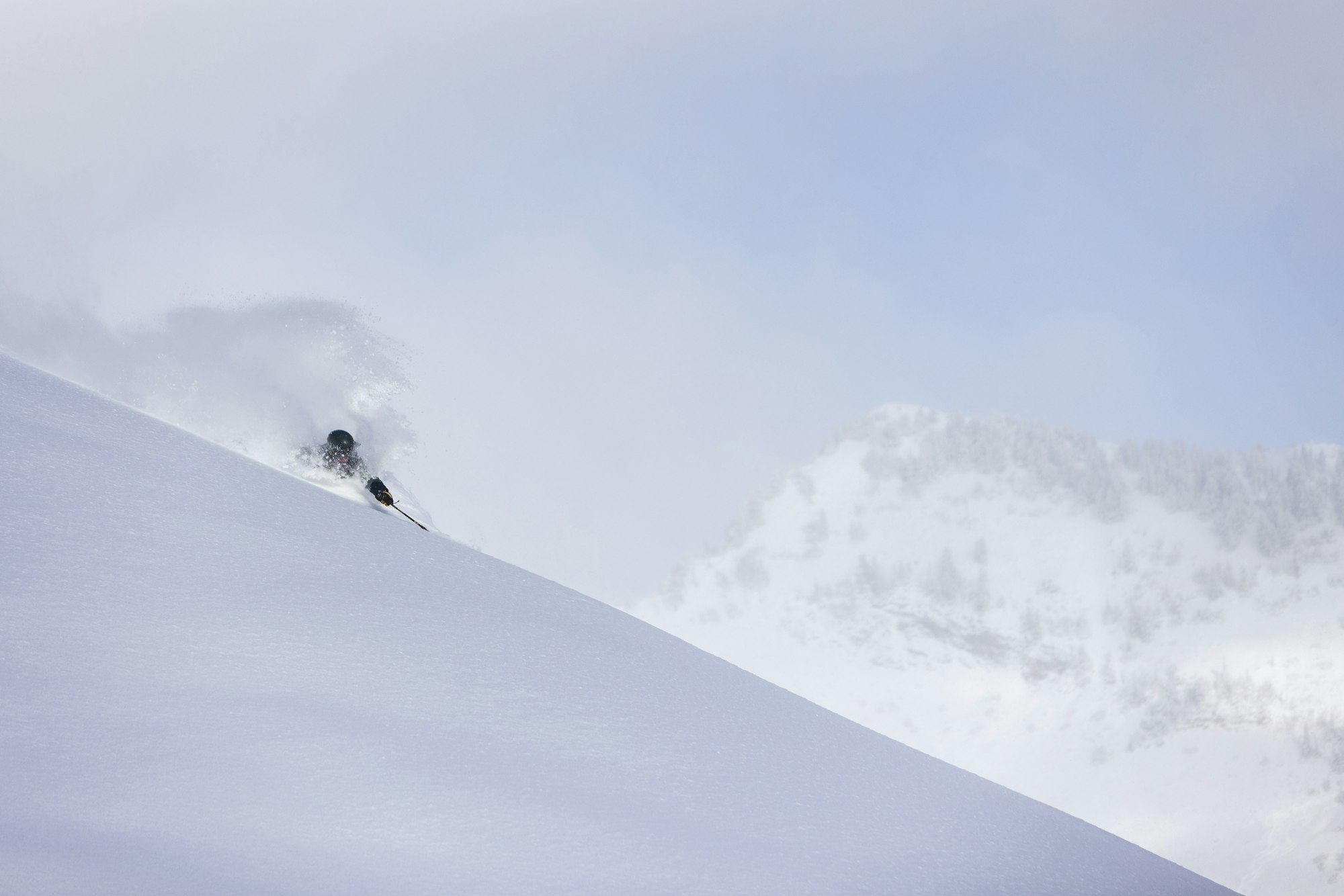 Skier Drew Gilmore skis through deep snow with mountains in the background