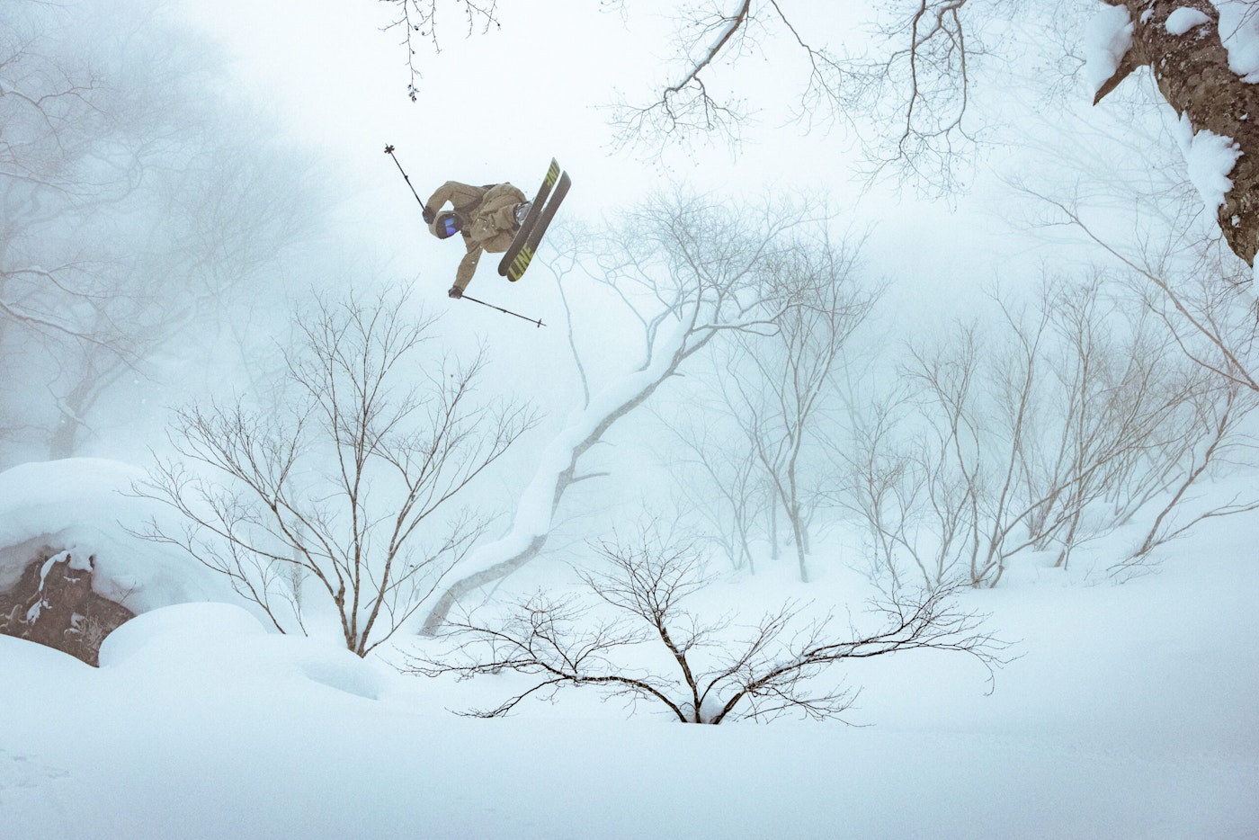 Skier Dylan Singers jumping high off a cliff in deep snow in the forest