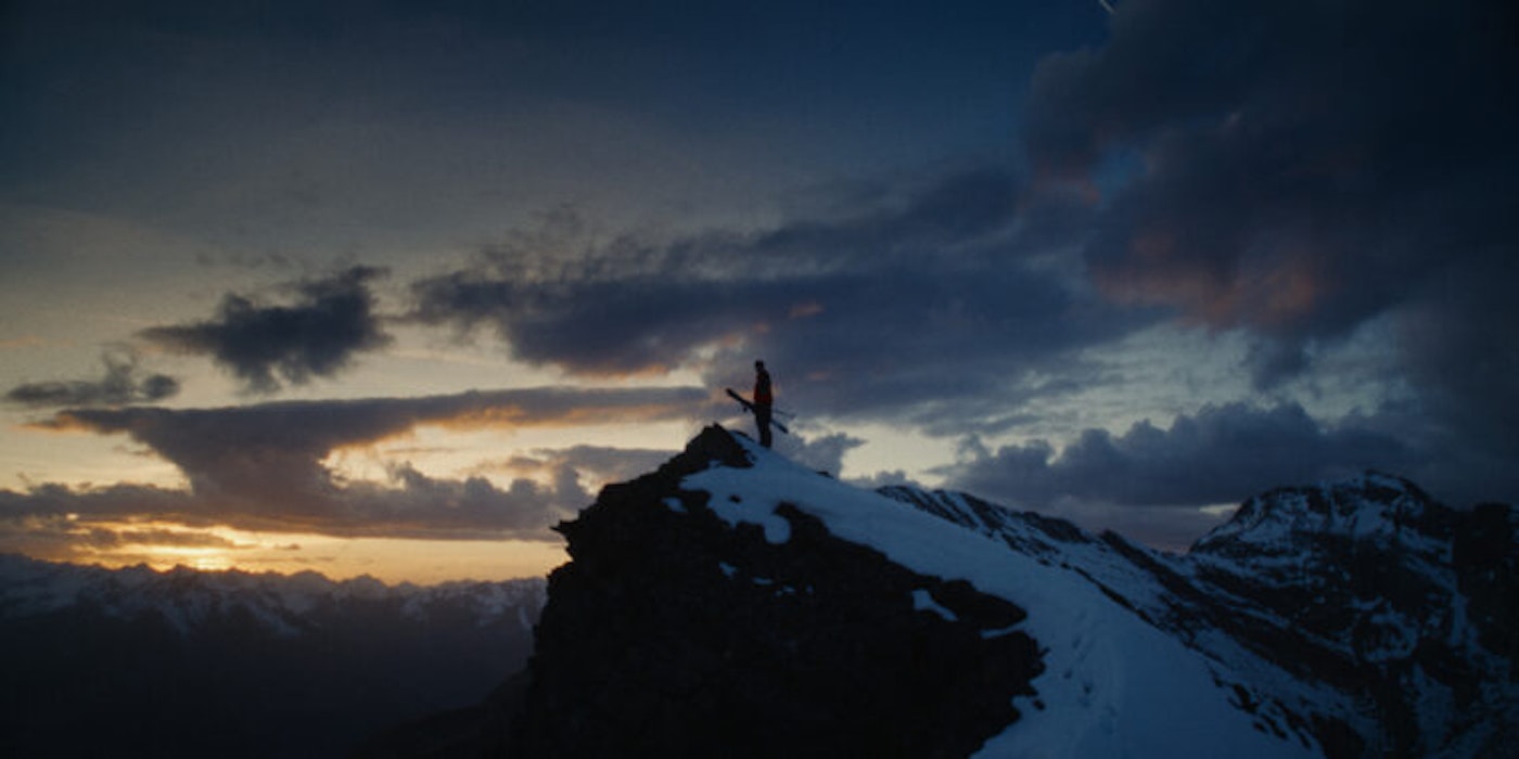 Skier stands on top of snowy peak at dusk