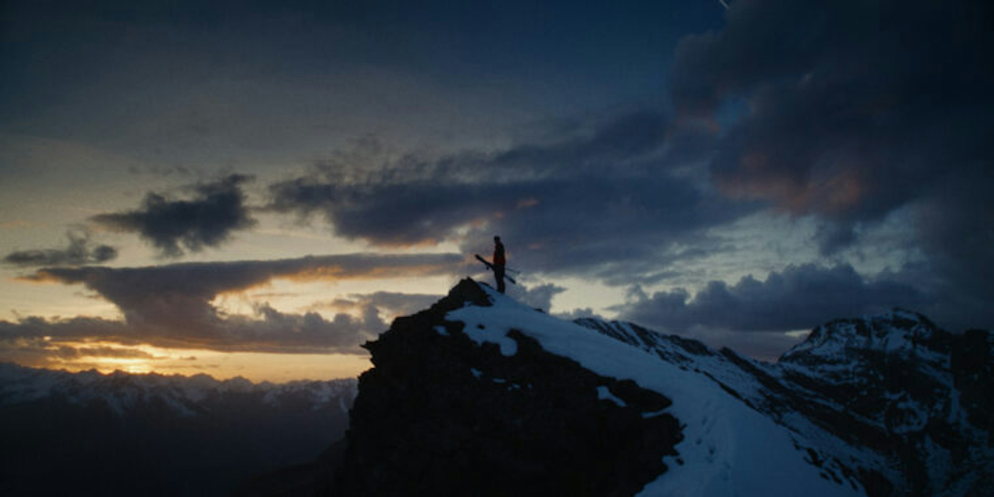Skier stands on top of snowy peak at dusk