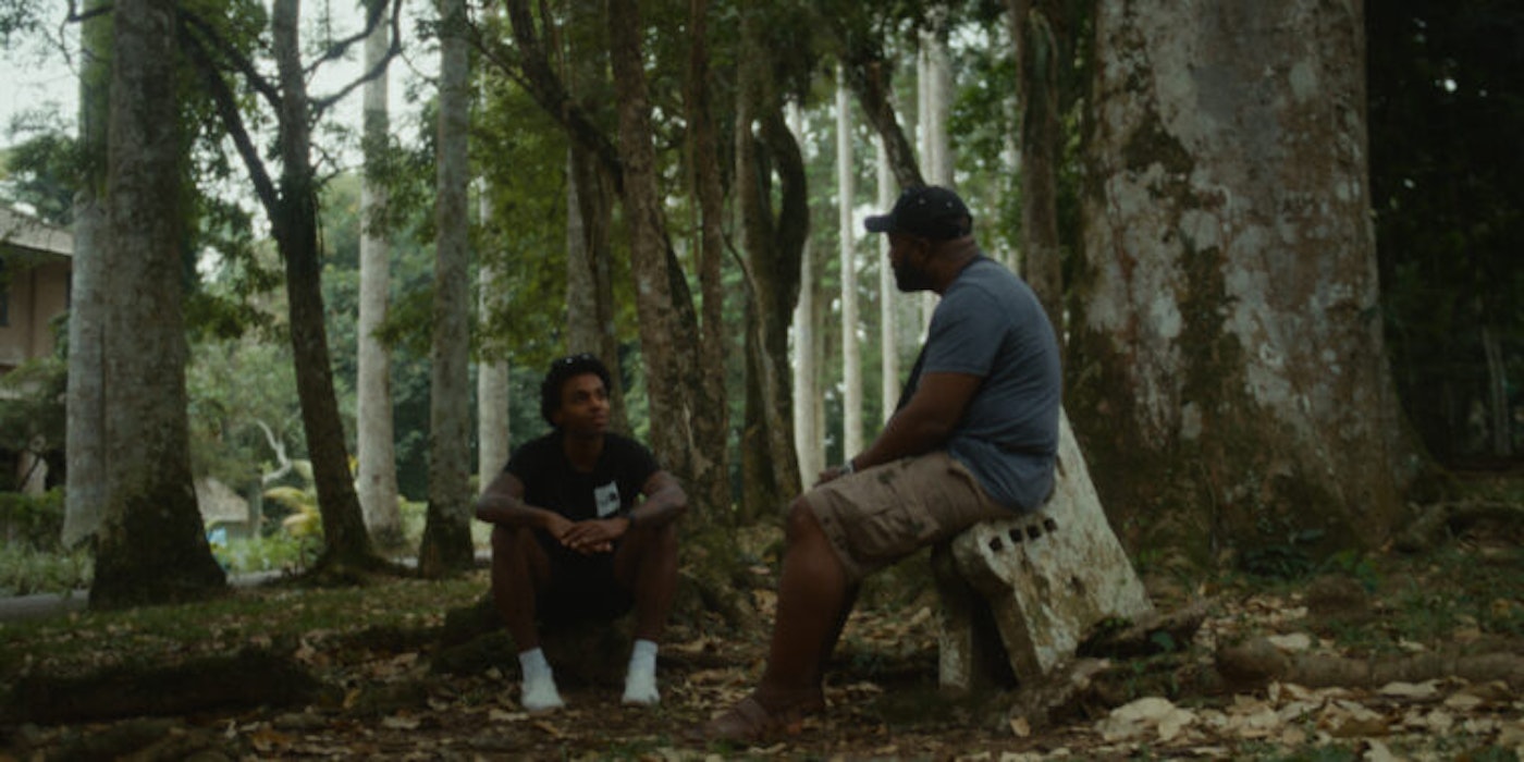 Dennis Ranalter sits with an older man in the forest discussing with him