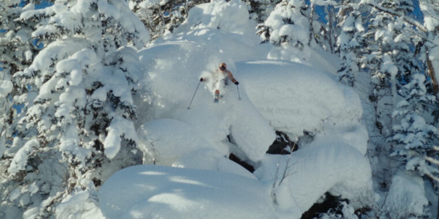 Skier jumps off of cliff with deep snow in the forest