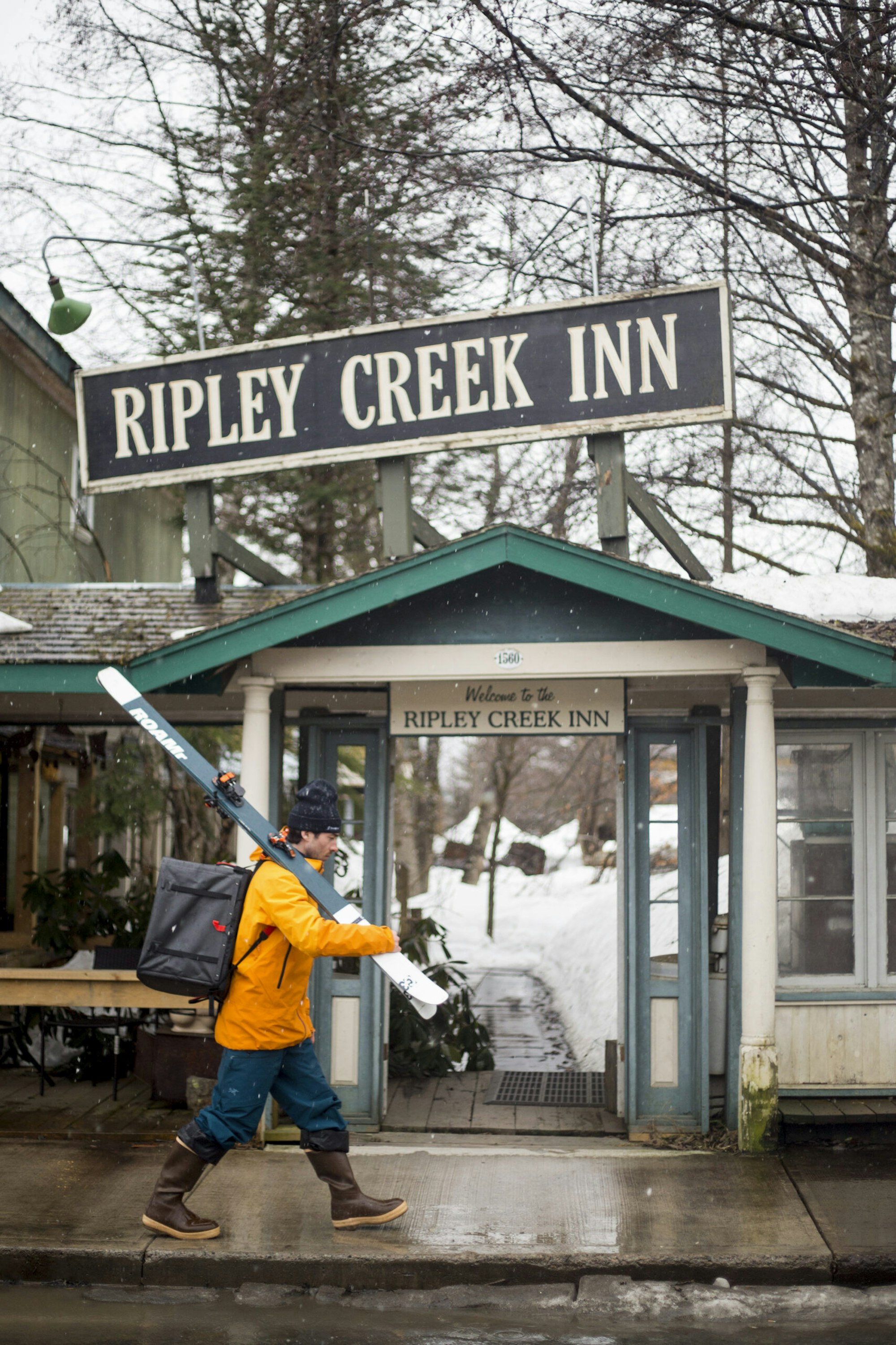 Jaret Bull carrying skis past an inn in Stewart, BC
