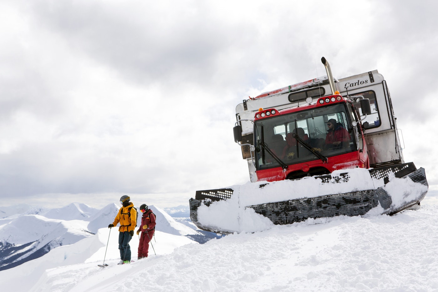 Skiers Yuki Tsubota and Jaret Bull standing in deep snow by a snowcat on top of a mountain in Smithers, BC