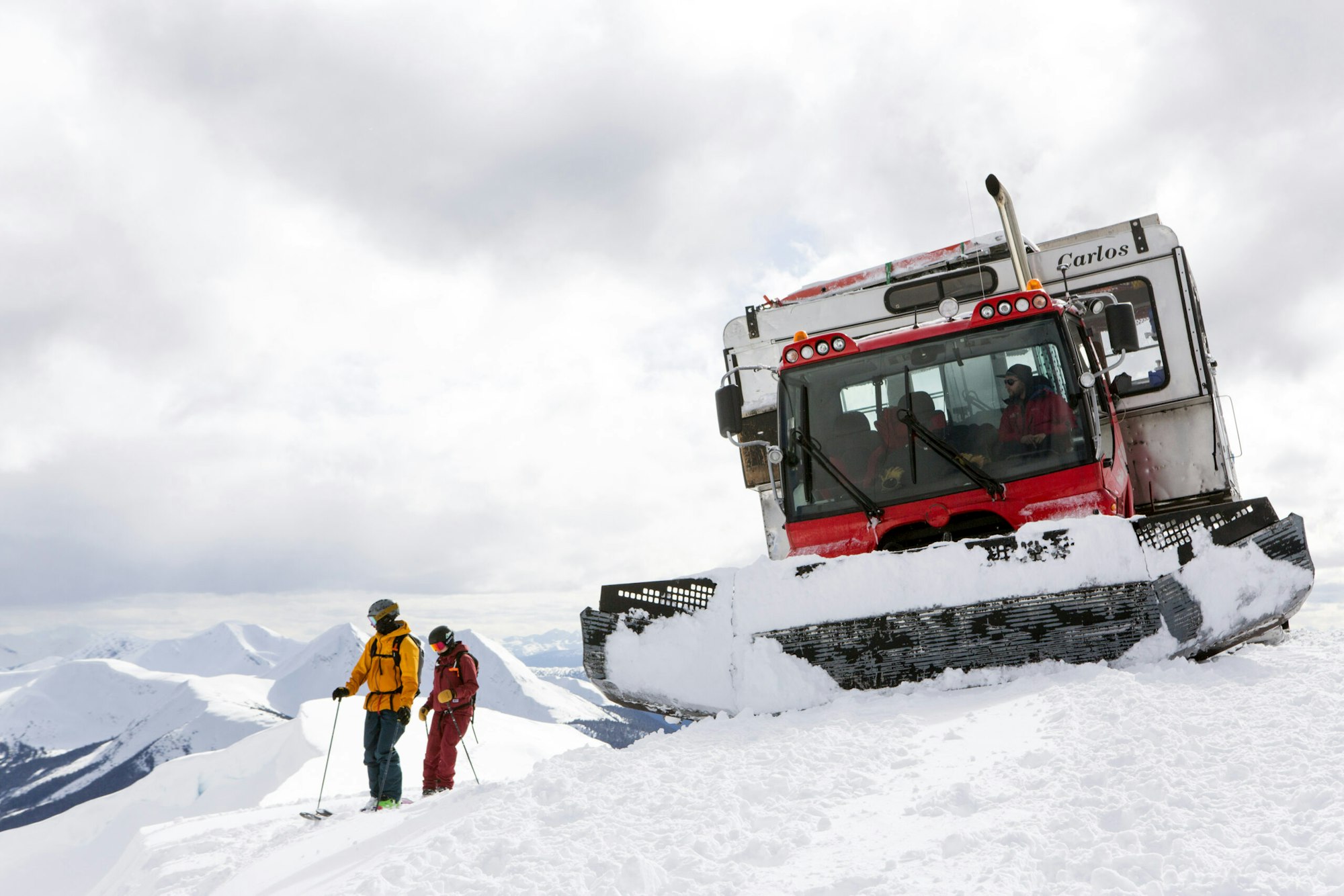 Skiers Yuki Tsubota and Jaret Bull standing in deep snow by a snowcat on top of a mountain in Smithers, BC