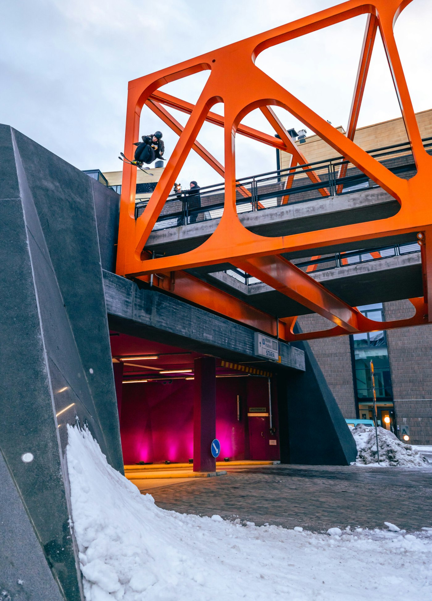 Skier Mainio Ormio jumping through a hole in the side of a bridge onto snow on the ground