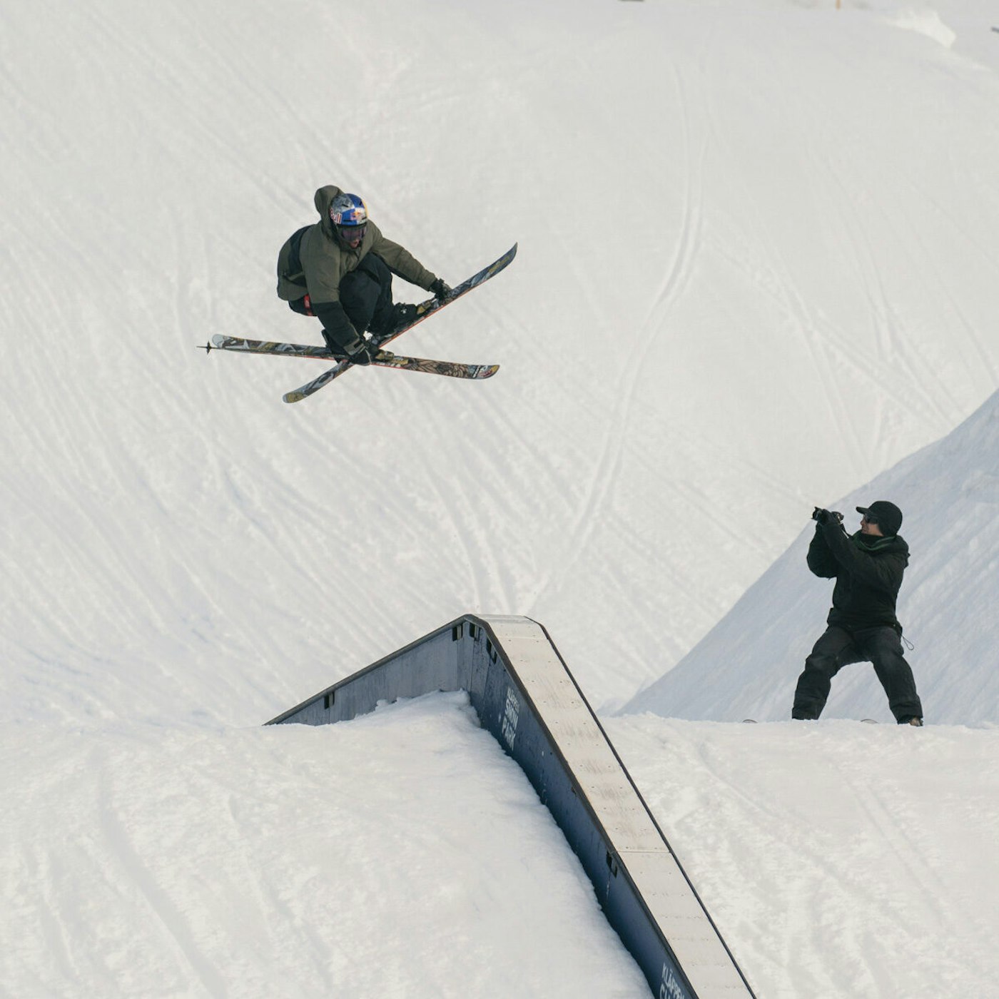 Skier Torin Yater-Wallace grabbing his skis mid air over a box with a Filmer below
