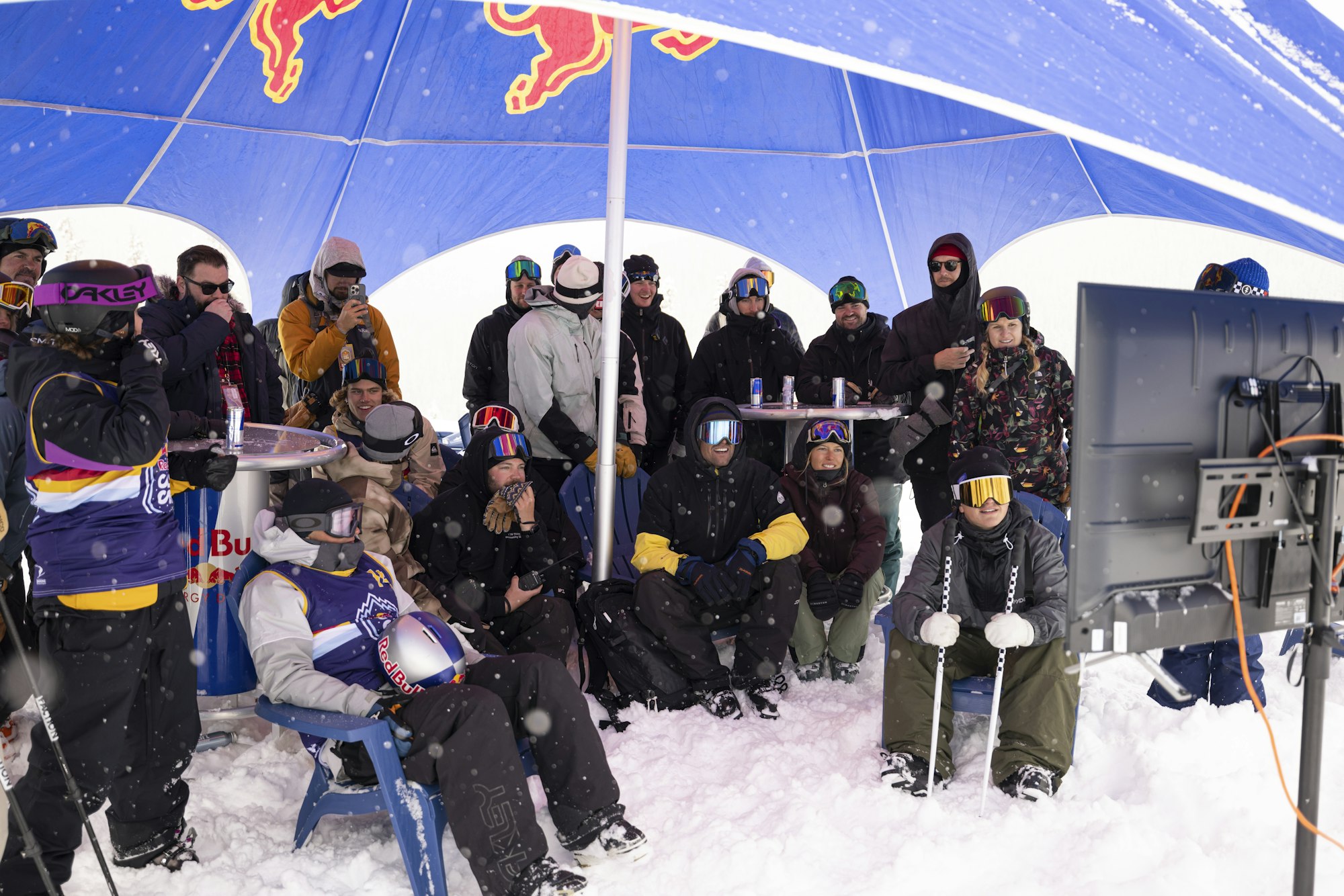 Skiers watch Red Bull cascade competition on a TV under a Red Bull tent in the snow