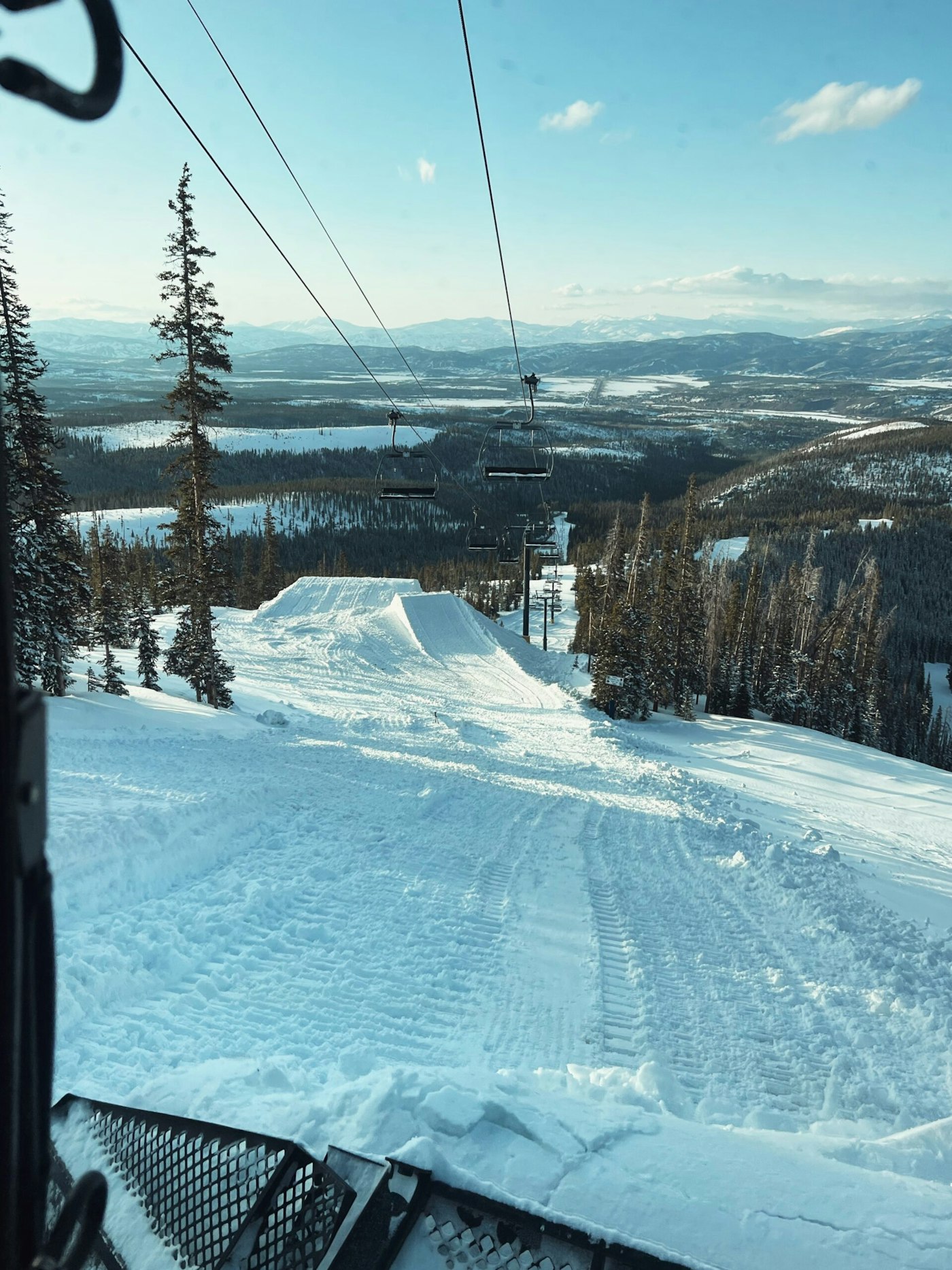 A snow cat working on building new terrain park features underneath a chairlift at winter park resort