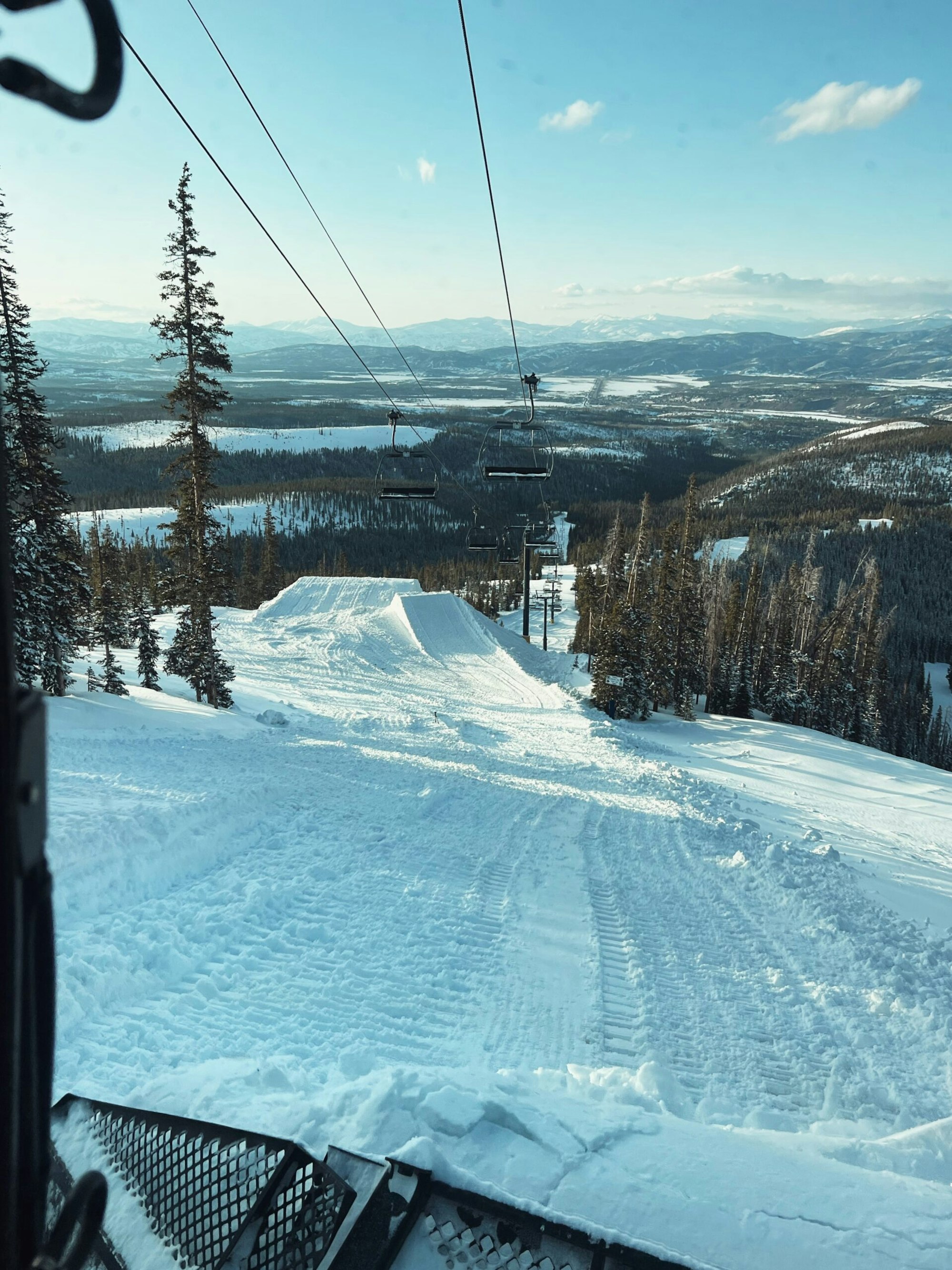 A snow cat working on building new terrain park features underneath a chairlift at winter park resort