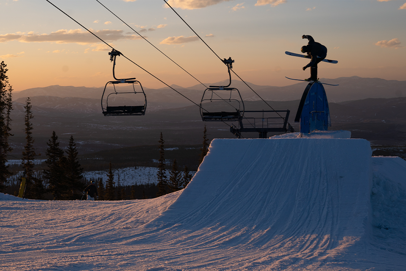 Skier Josh Conroy skis over a rainbow rail at dusk at Winter Park Resort
