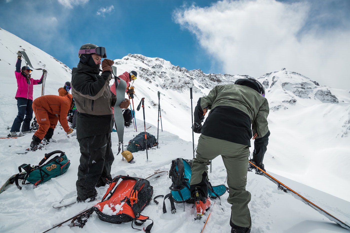 Skiers atop a snowy ridge remove the skins from their skis.