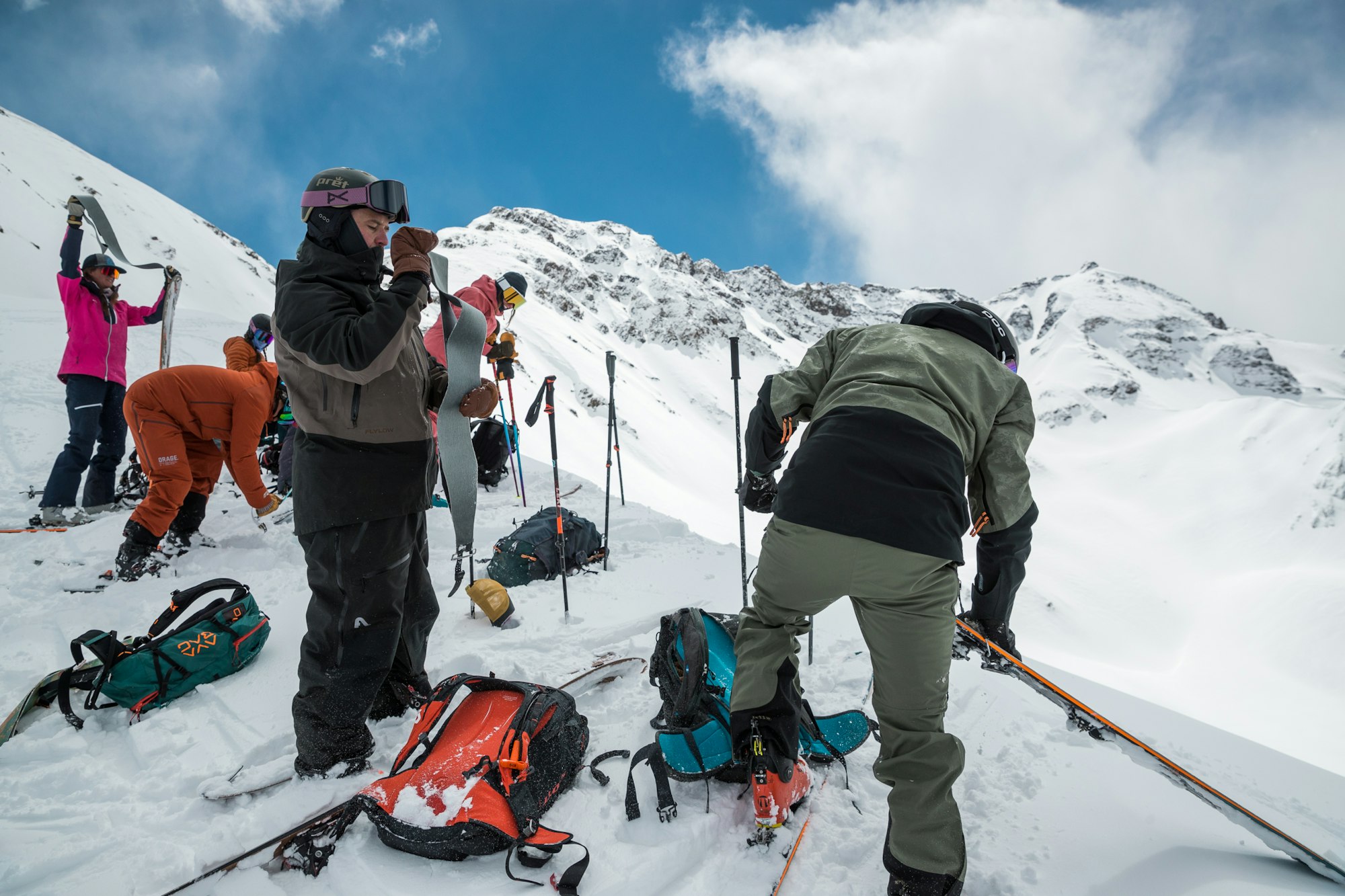 Skiers atop a snowy ridge remove the skins from their skis.