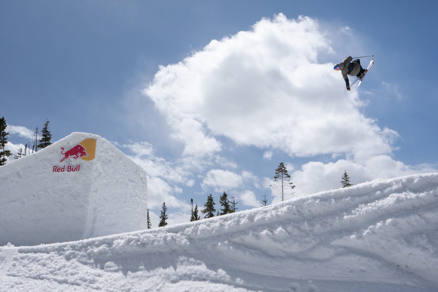 Skier mid air off a jump grabs the tails of their skis