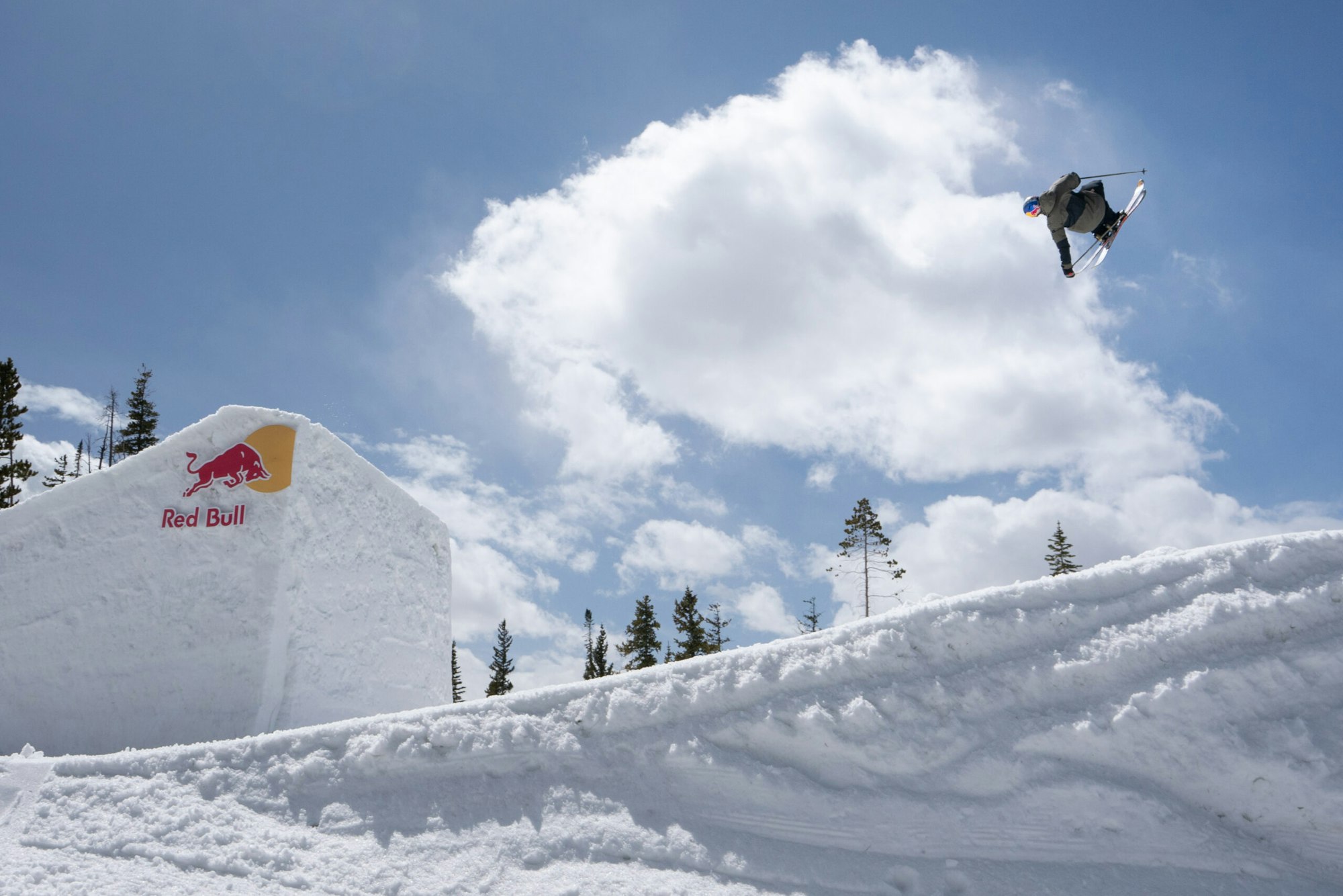 Skier mid air off a jump grabs the tails of their skis