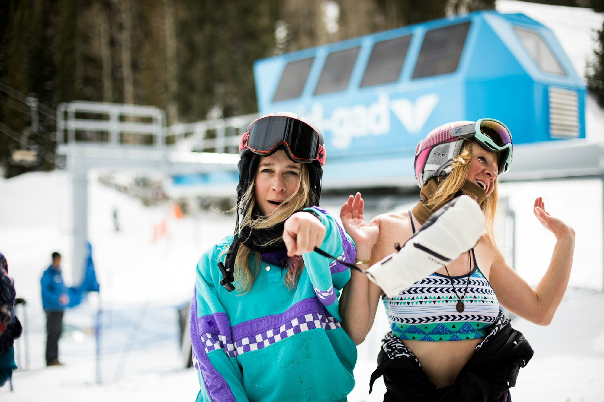 Skiers dressed in neon outfits smile and point at the camera