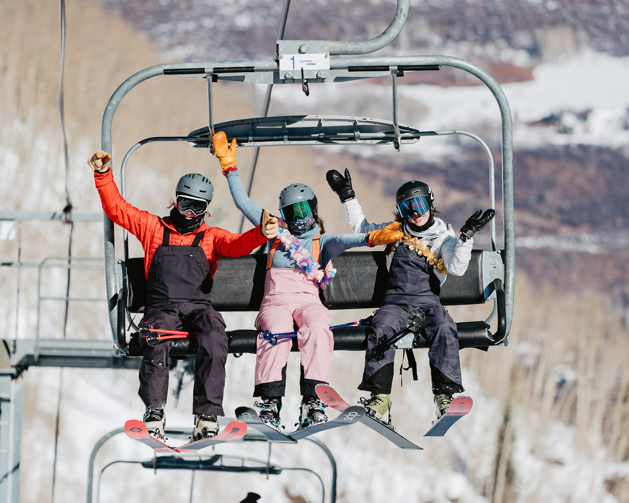 Three skiers sit on a chairlift with their hands in the air