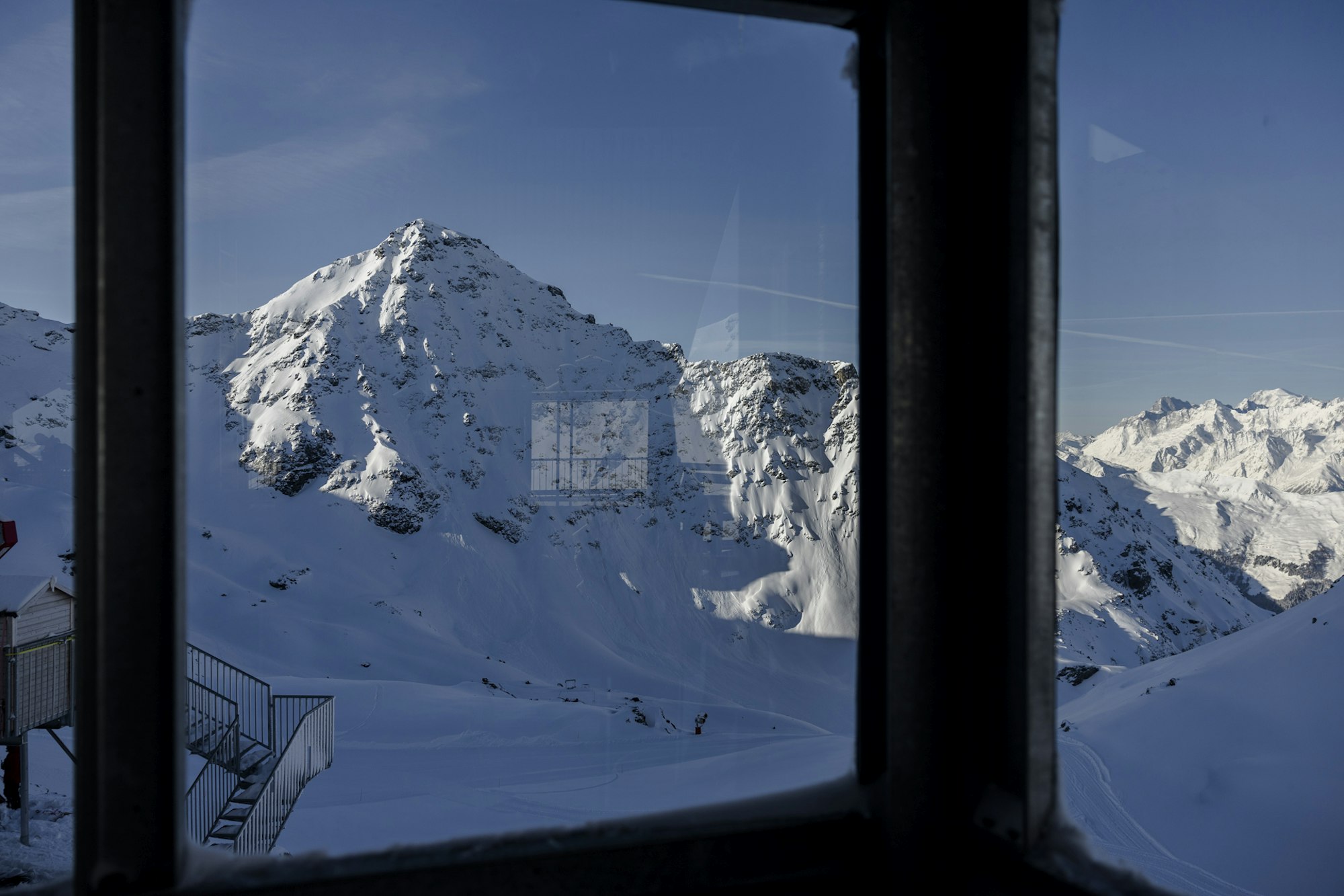 The snow covered Bed des Rosses from a window under a blue sky