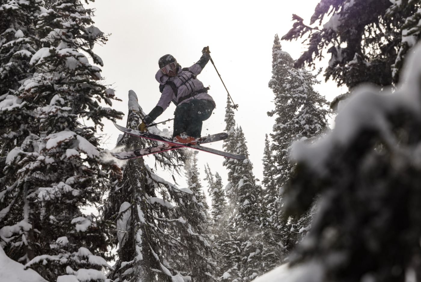 Caite Zeliff grabbing her skis in the air mid jump in a snowy forest