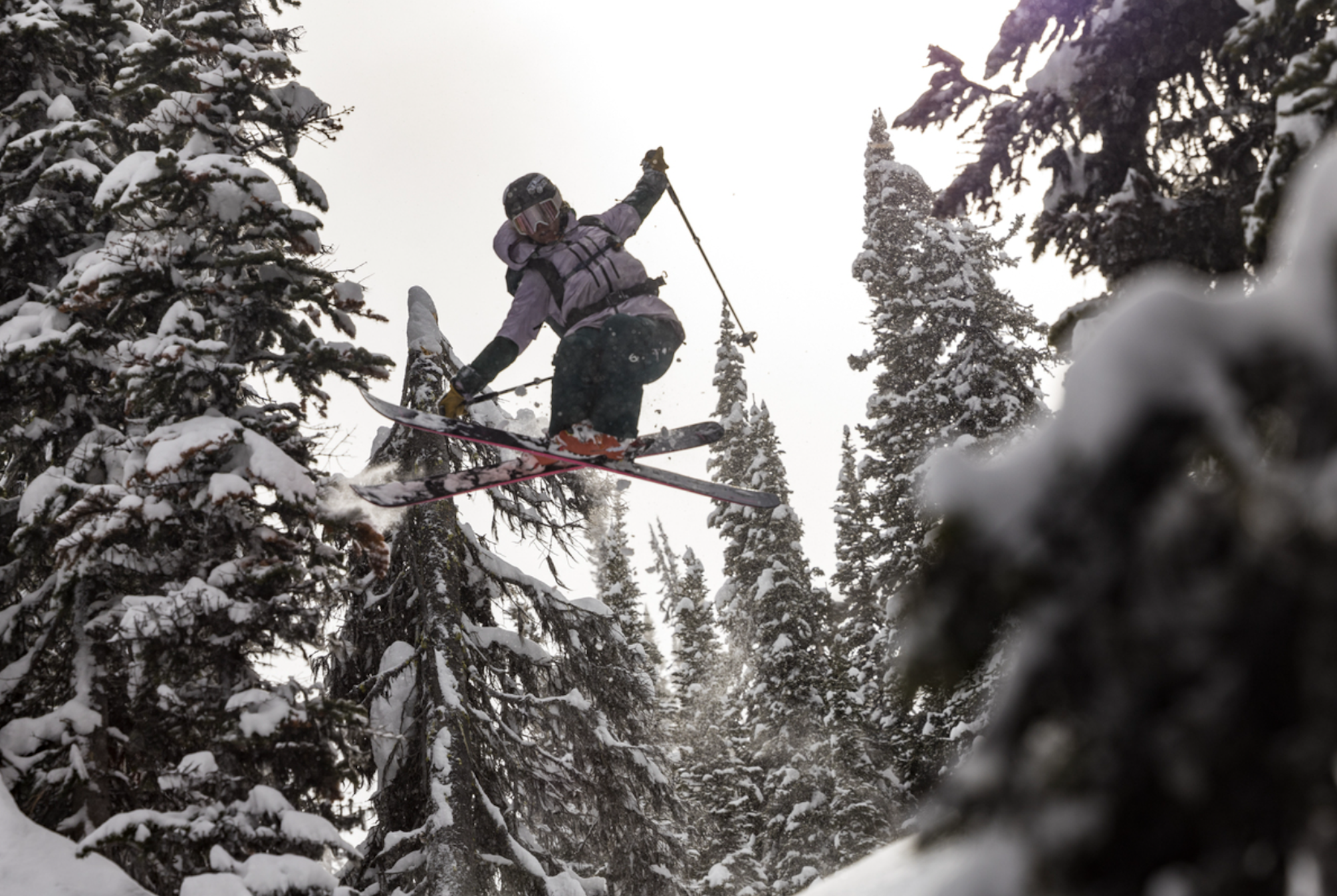 Caite Zeliff grabbing her skis in the air mid jump in a snowy forest