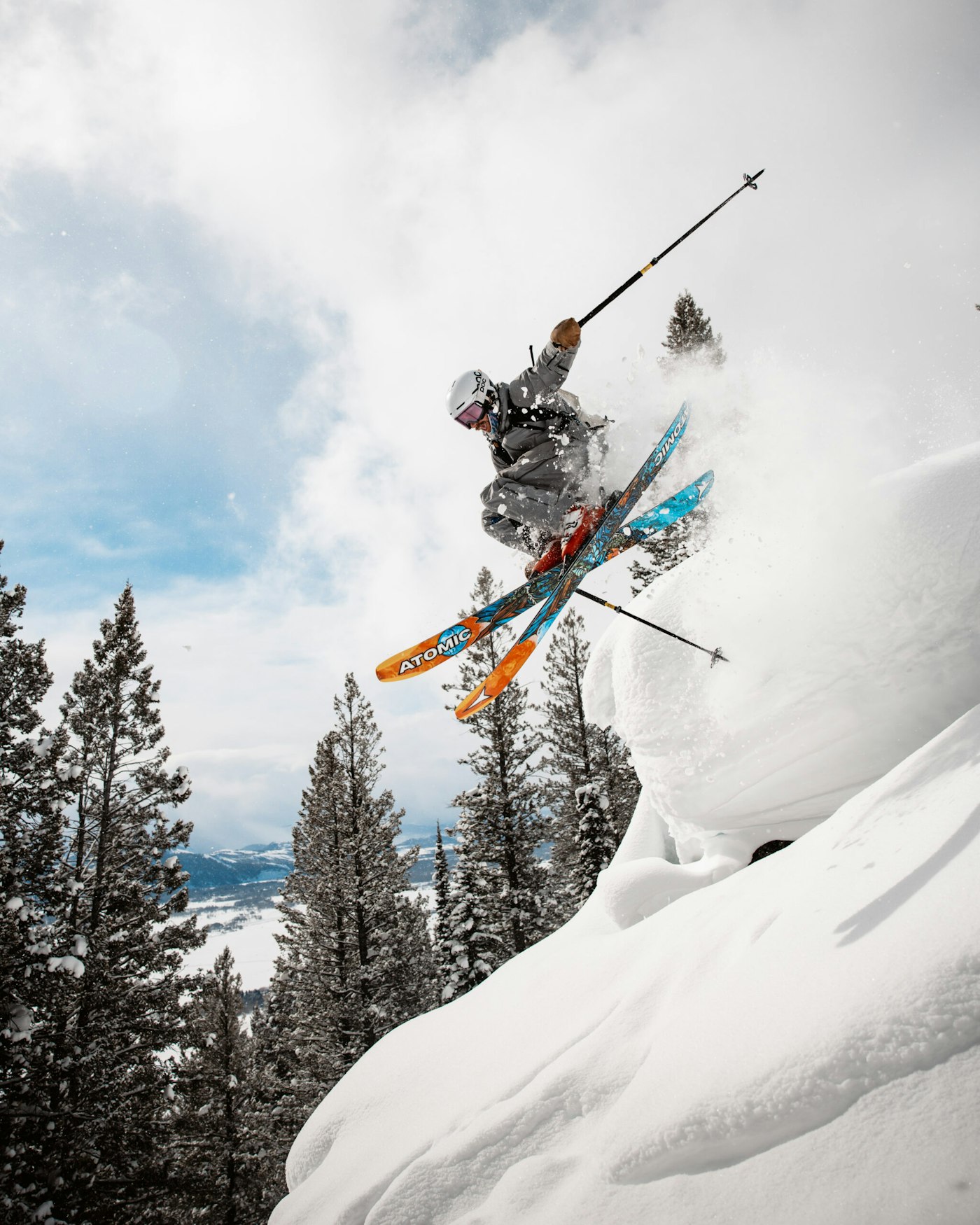 Skier on atomic skis jumping off a snowy cliff into deep snow