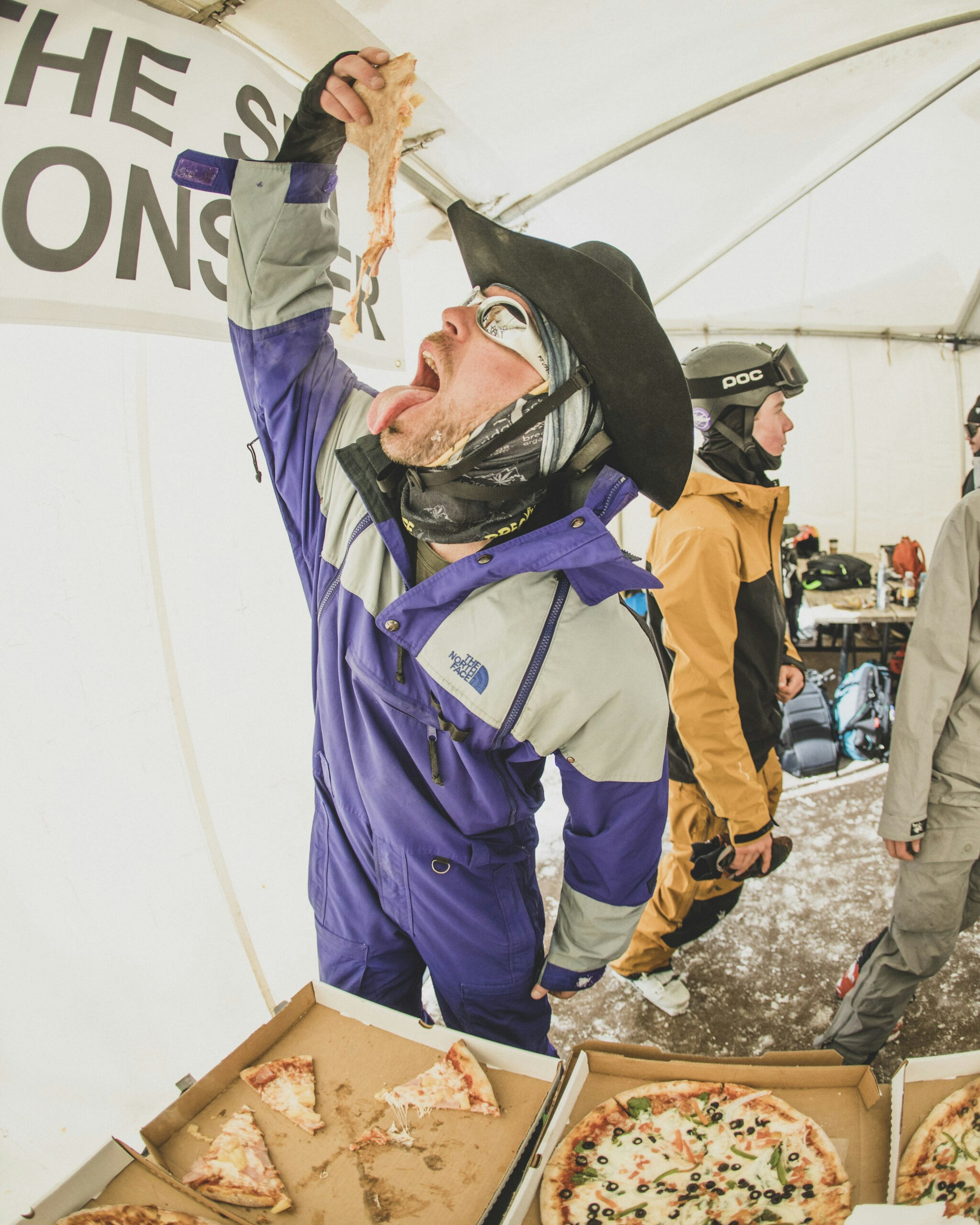 Man in ski clothes eating a slice of pizza