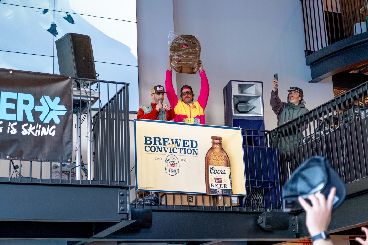 man holds coors branded backpack in the air