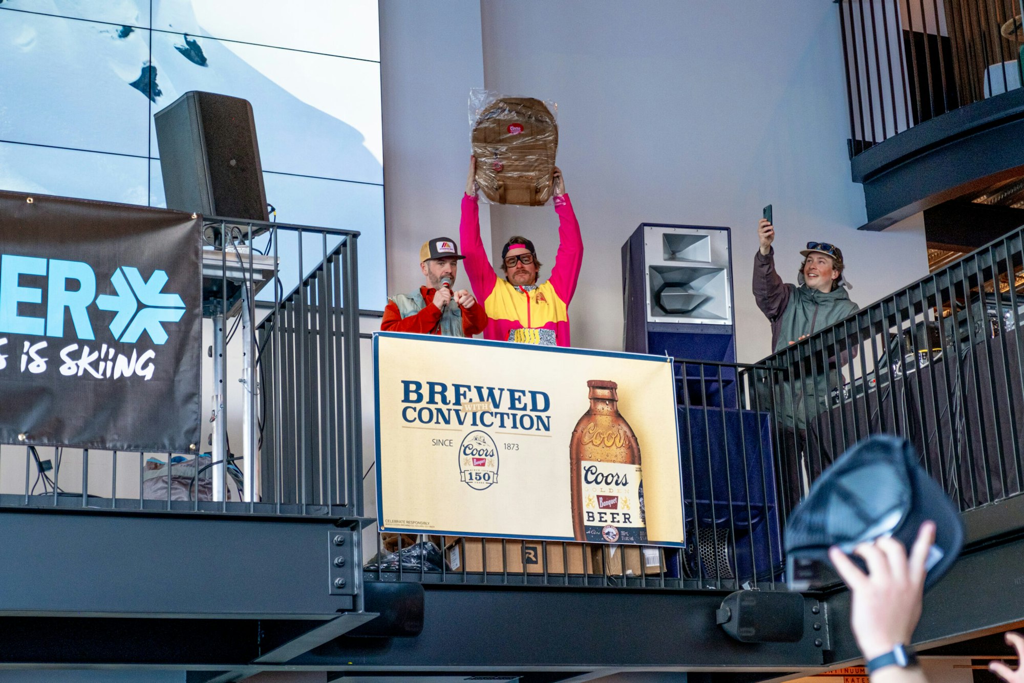 man holds coors branded backpack in the air