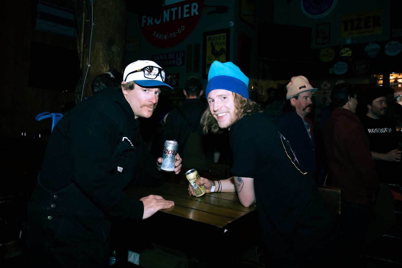 Two men sit at a bar with coors beers