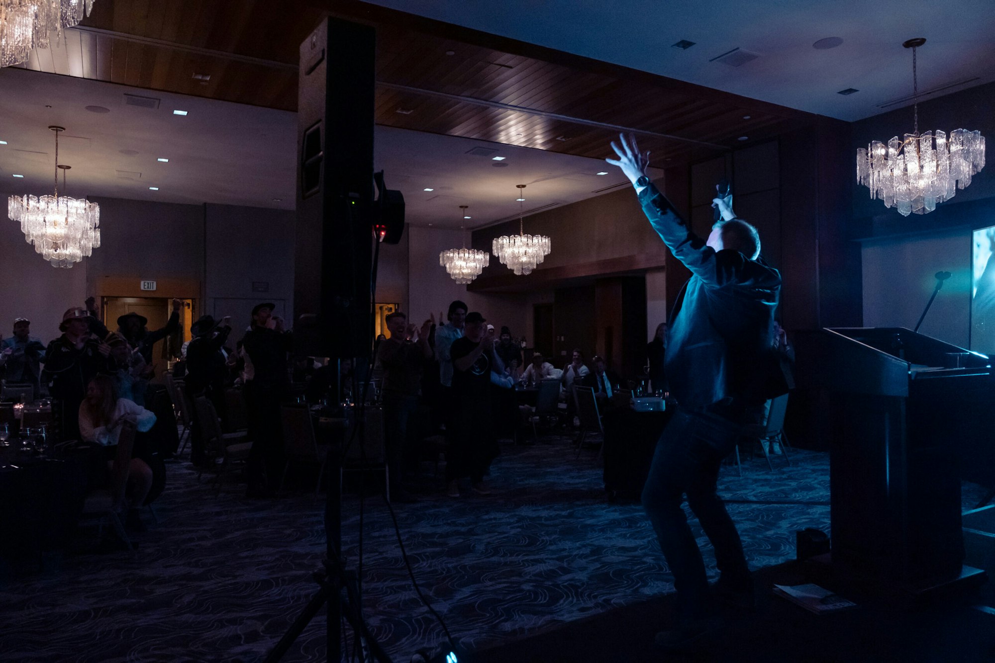 A man stands on a stage in front of people and raises his hands