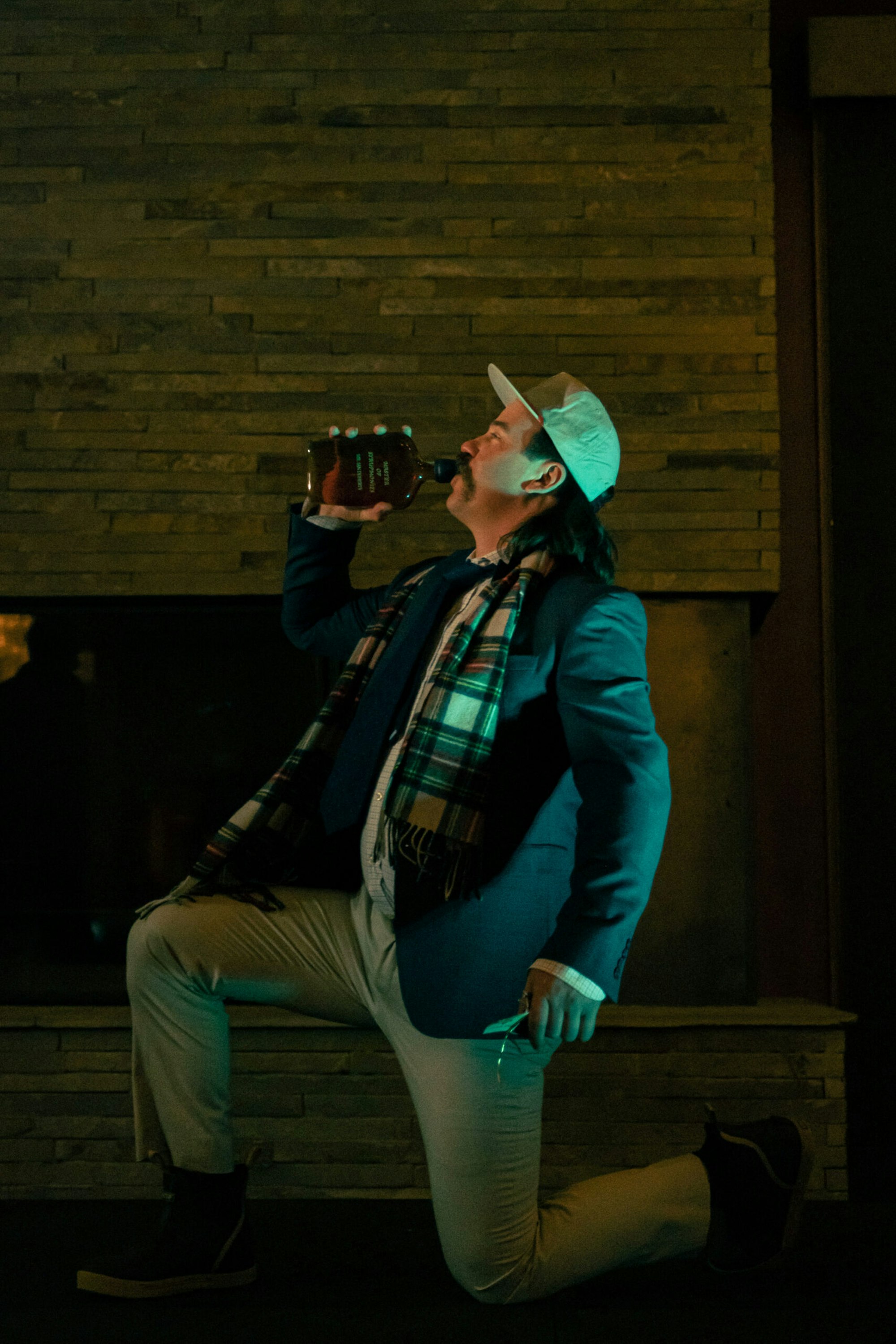 a man kneels on one knee and drinks out of a dark bottle