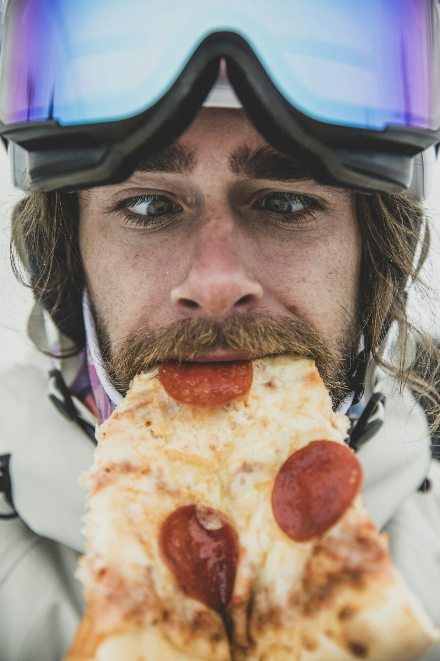 A skier takes a bite of a slice of pizza