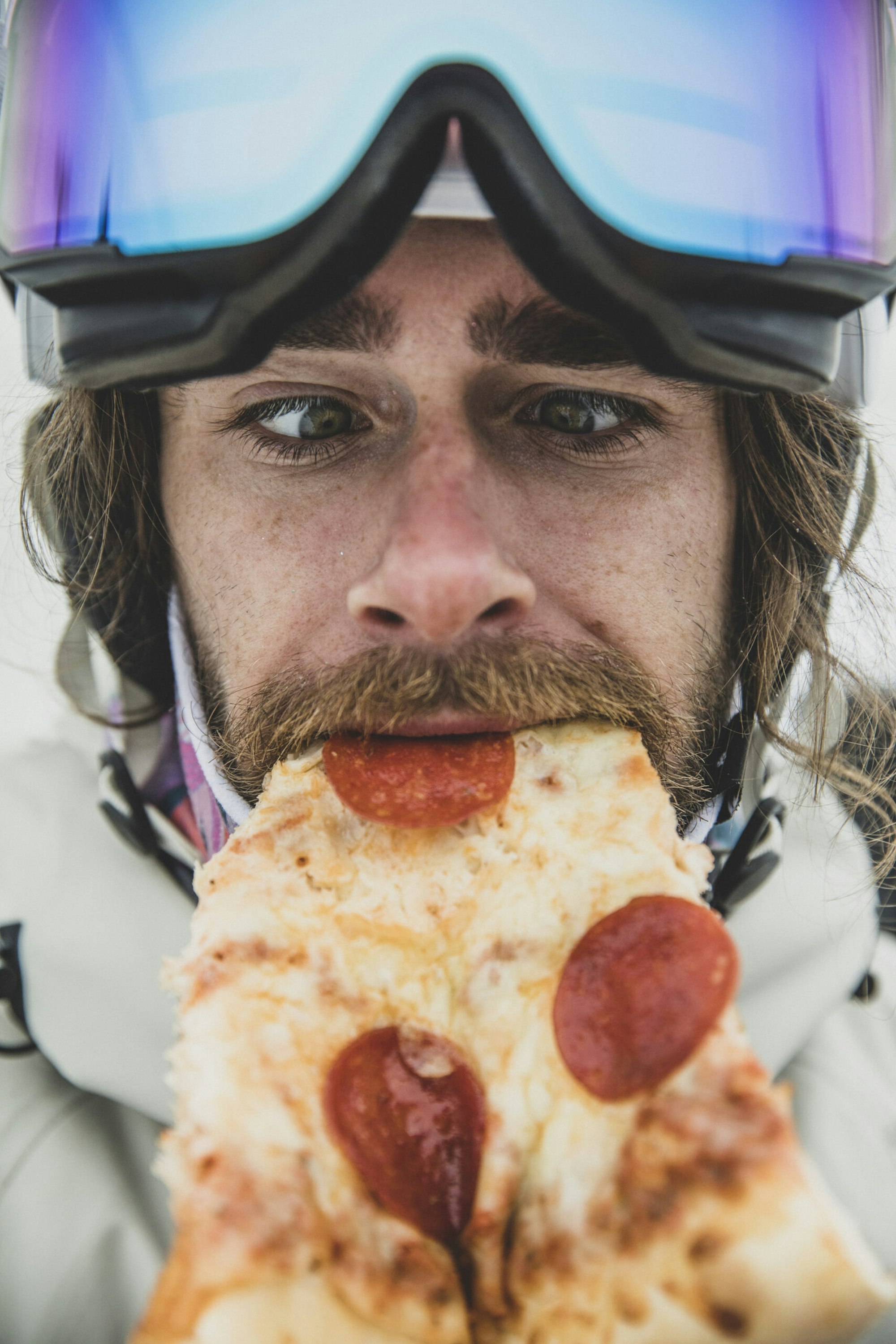A skier takes a bite of a slice of pizza
