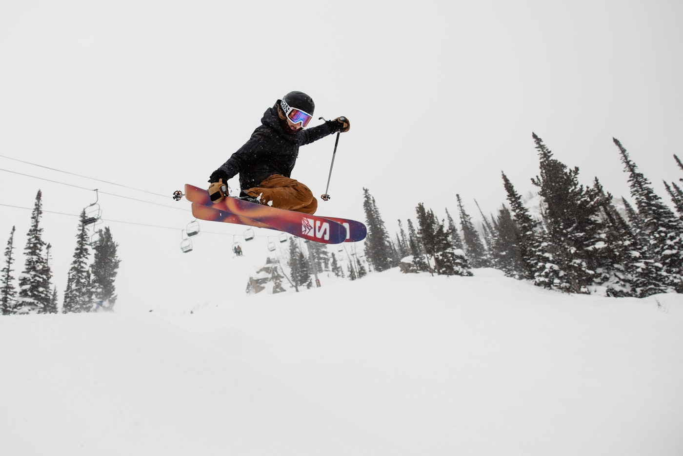 Skier catches air and grabs the side of their skis in deep snow