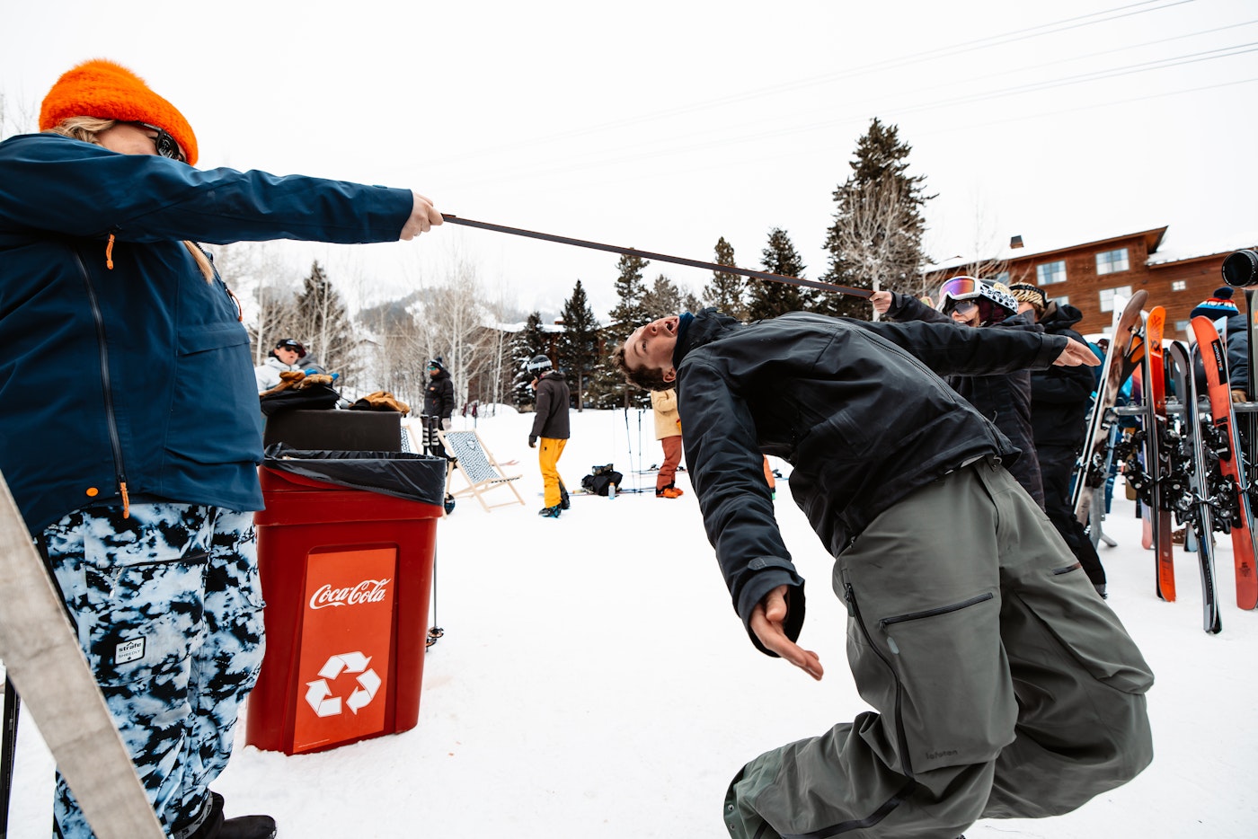 Skiers play limbo outside with a ski pole