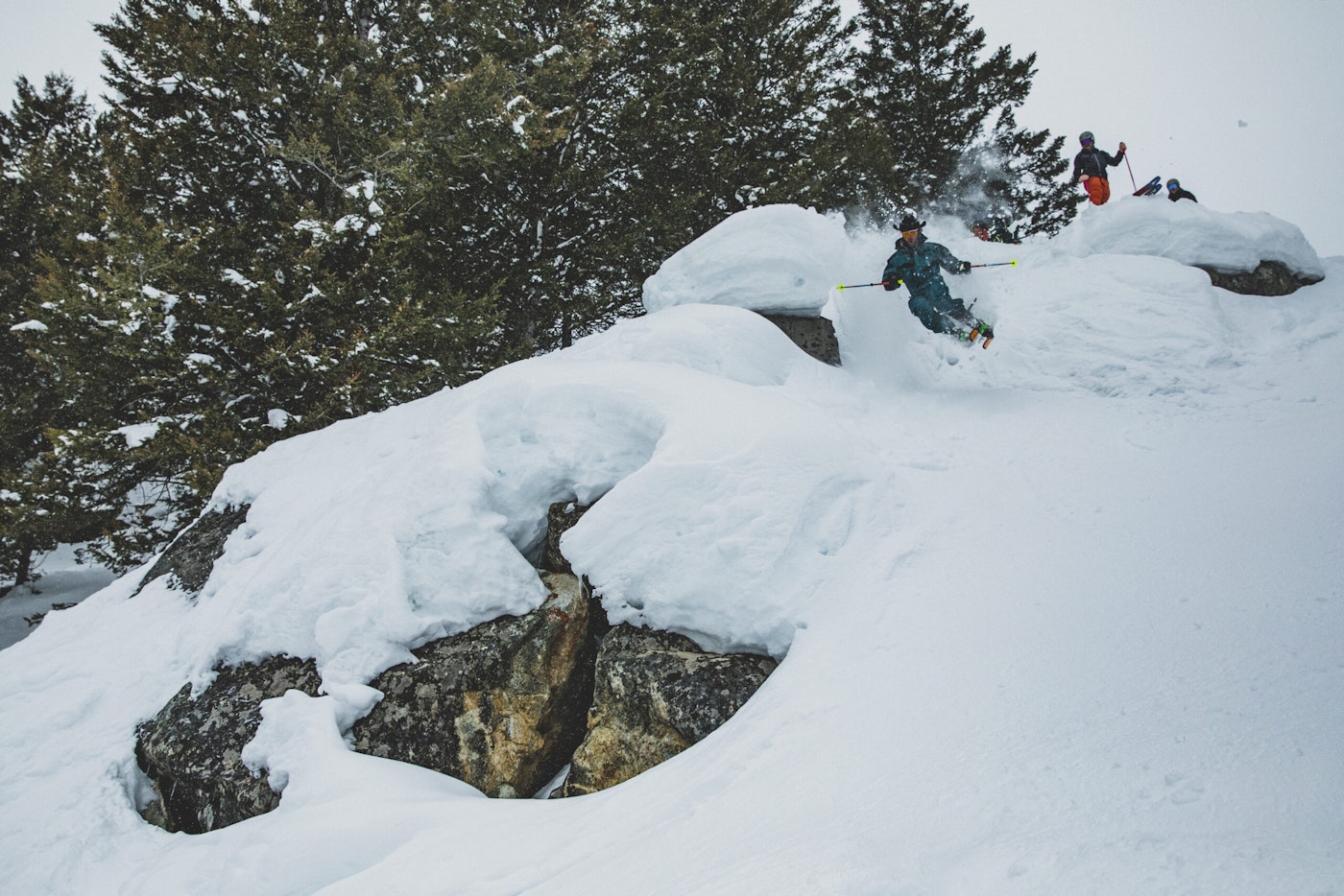 Skiers ski off snowy rocks in deep snow