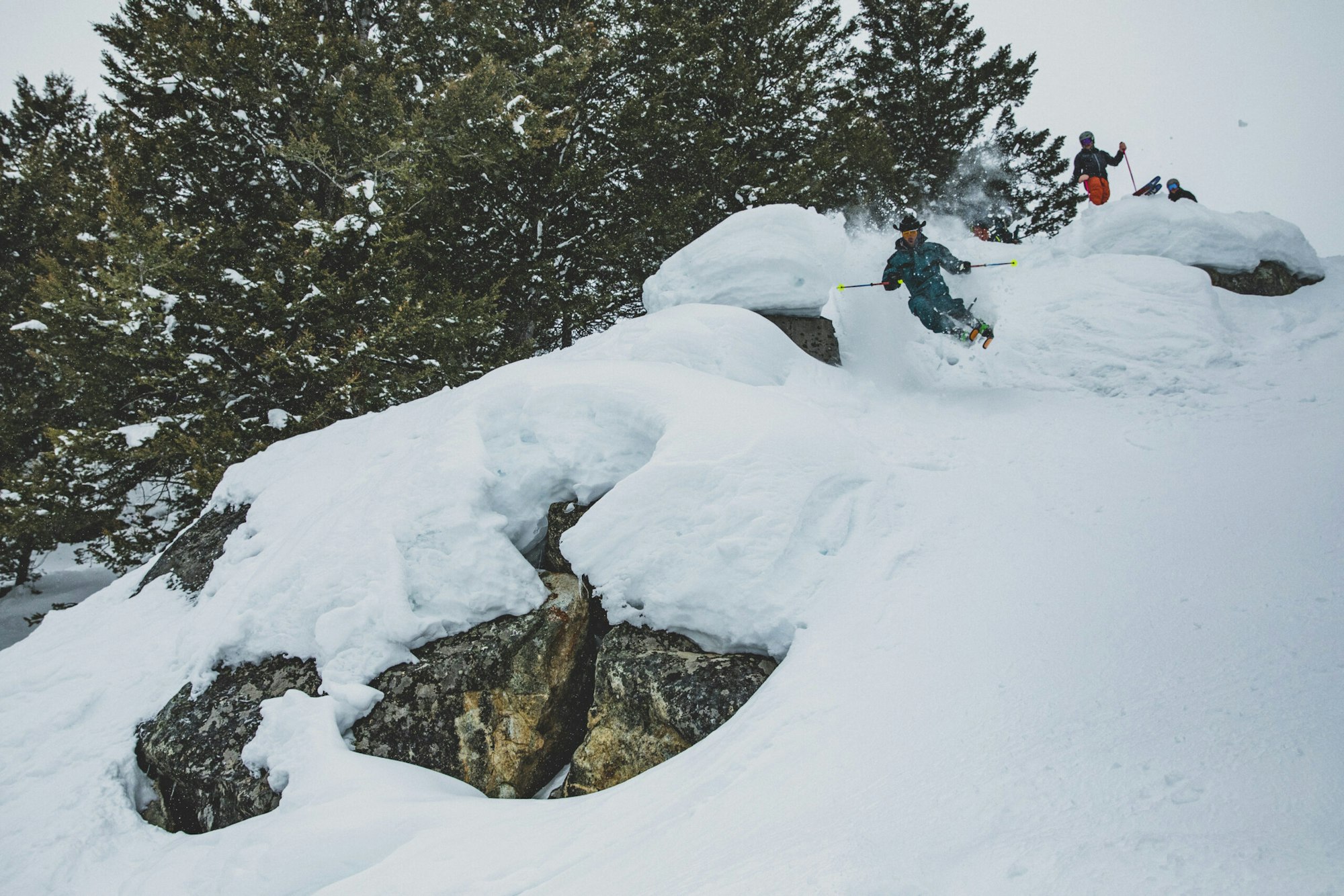 Skiers ski off snowy rocks in deep snow