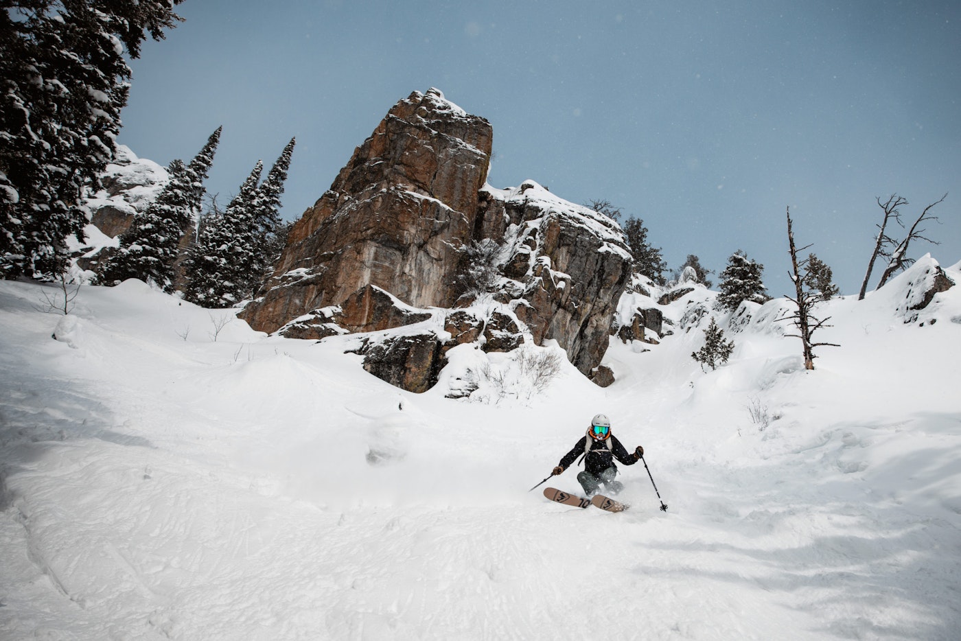 Skier skis down a steep slope below a massive rock cliff