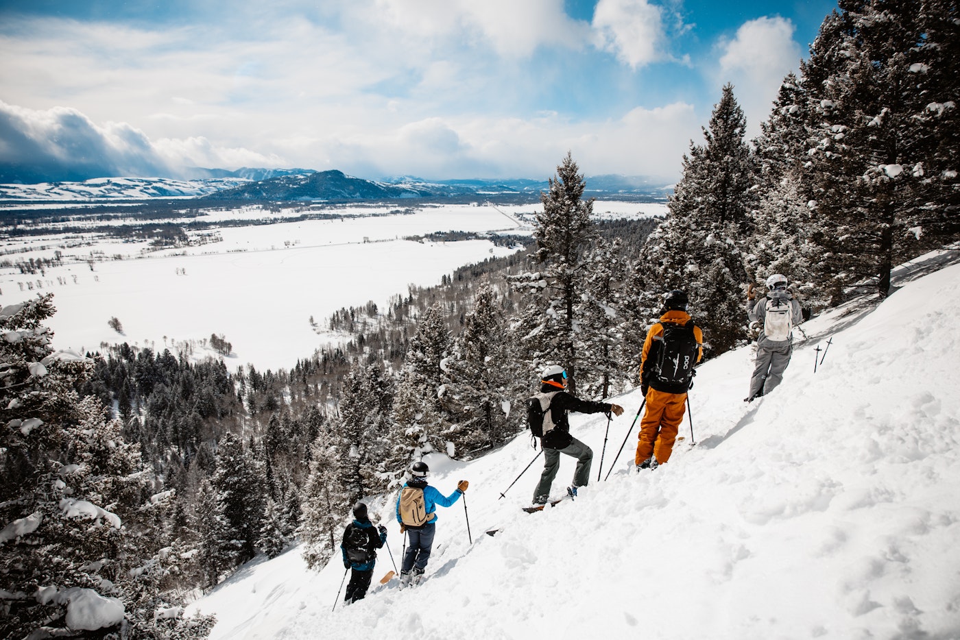 5 skiers stand on a steep slope looking off the mountain