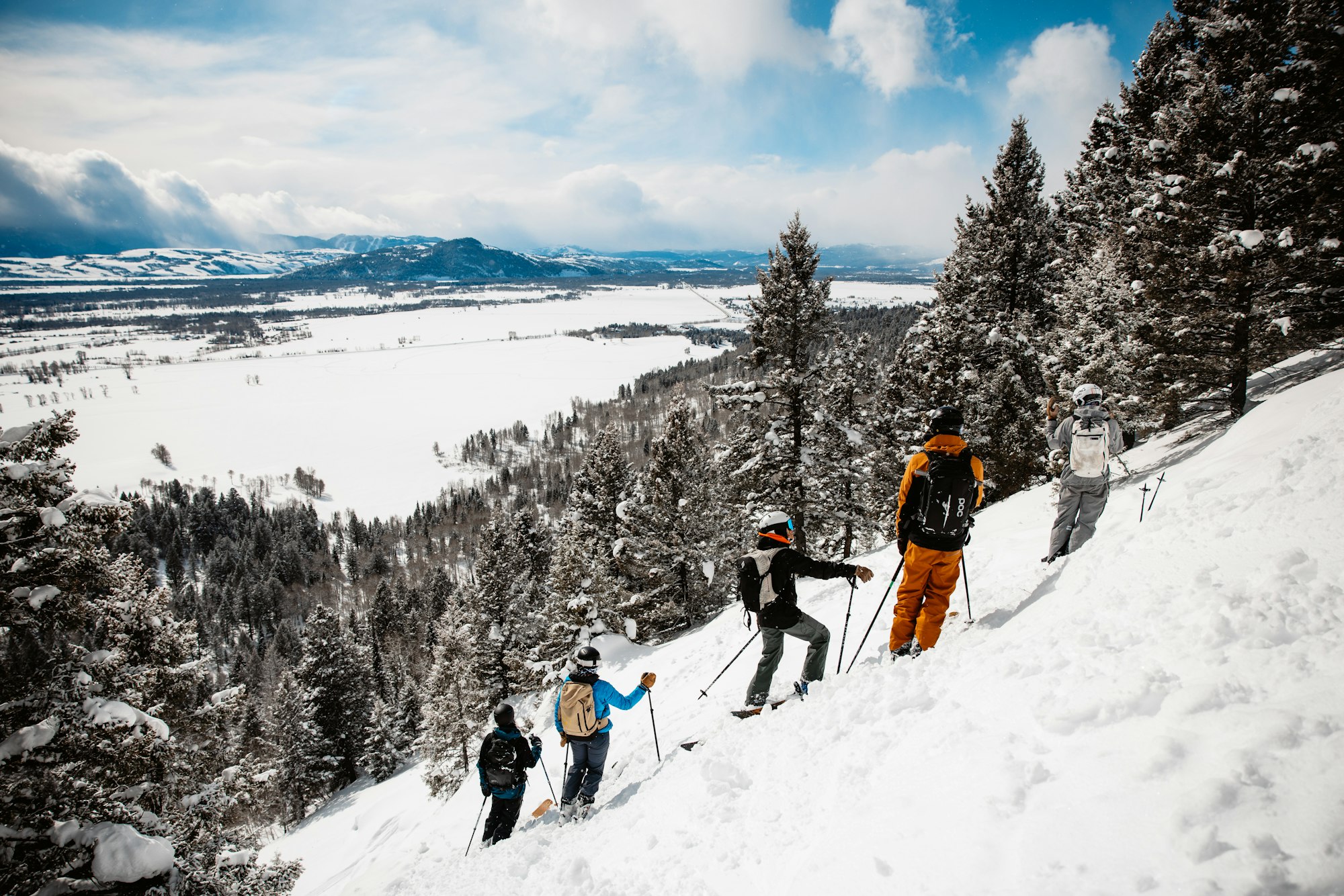 5 skiers stand on a steep slope looking off the mountain