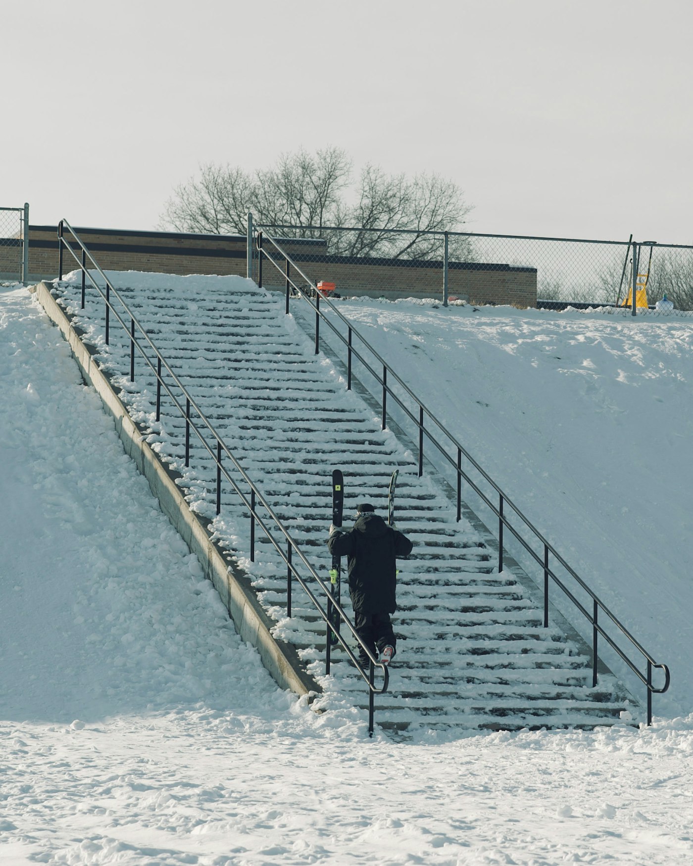 Skier hikes up an outdoor stairway carrying skis