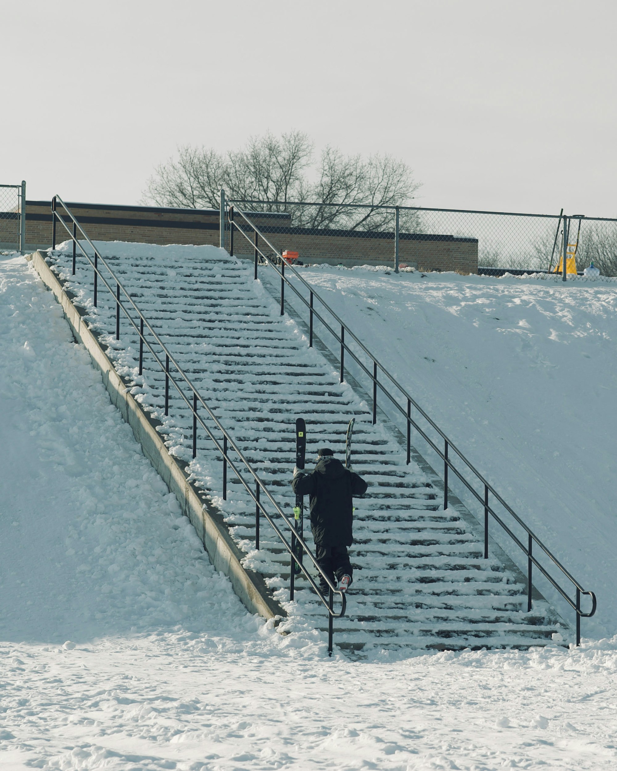 Skier hikes up an outdoor stairway carrying skis