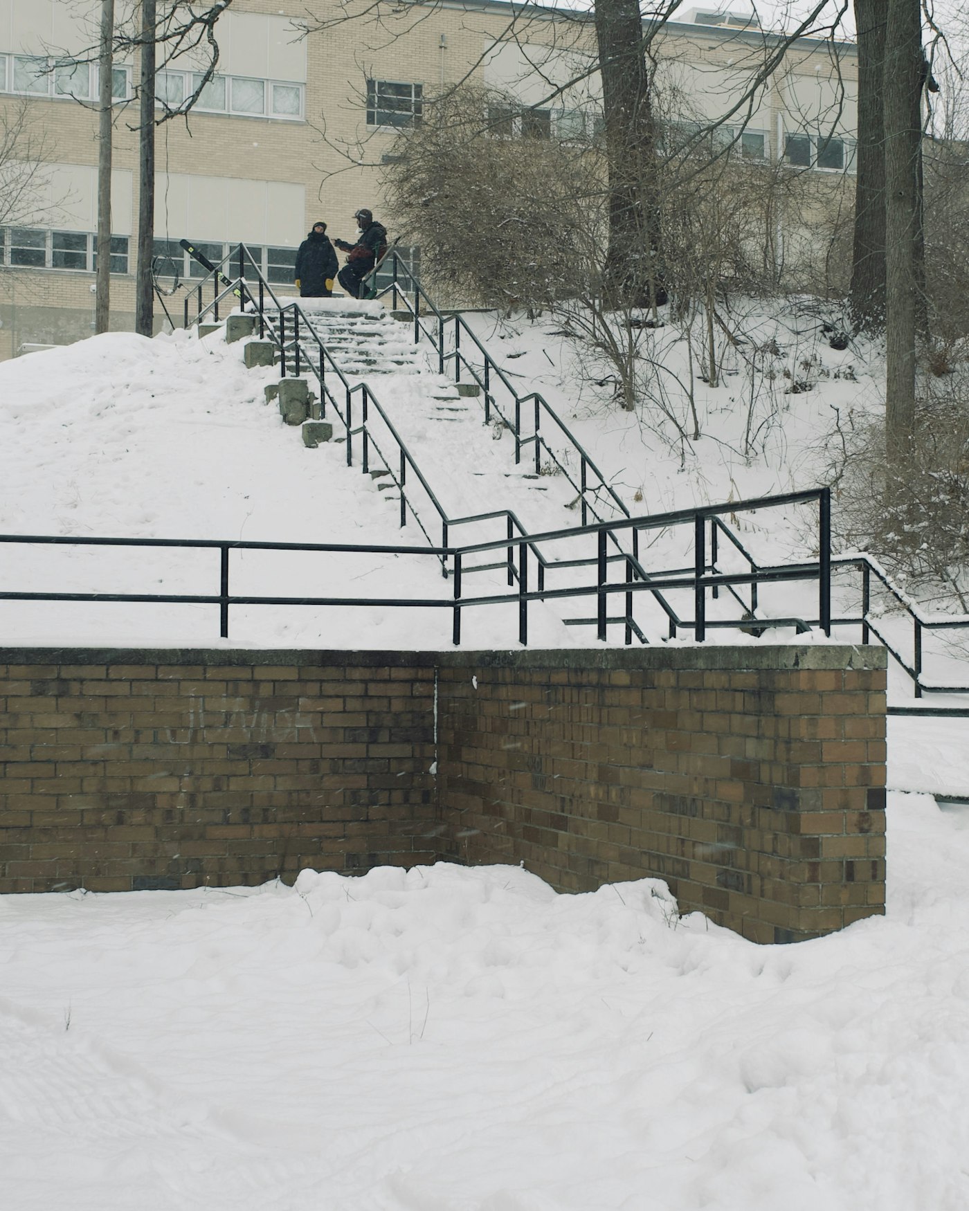 Skiers sit at the top of a snowy outdoor staircase