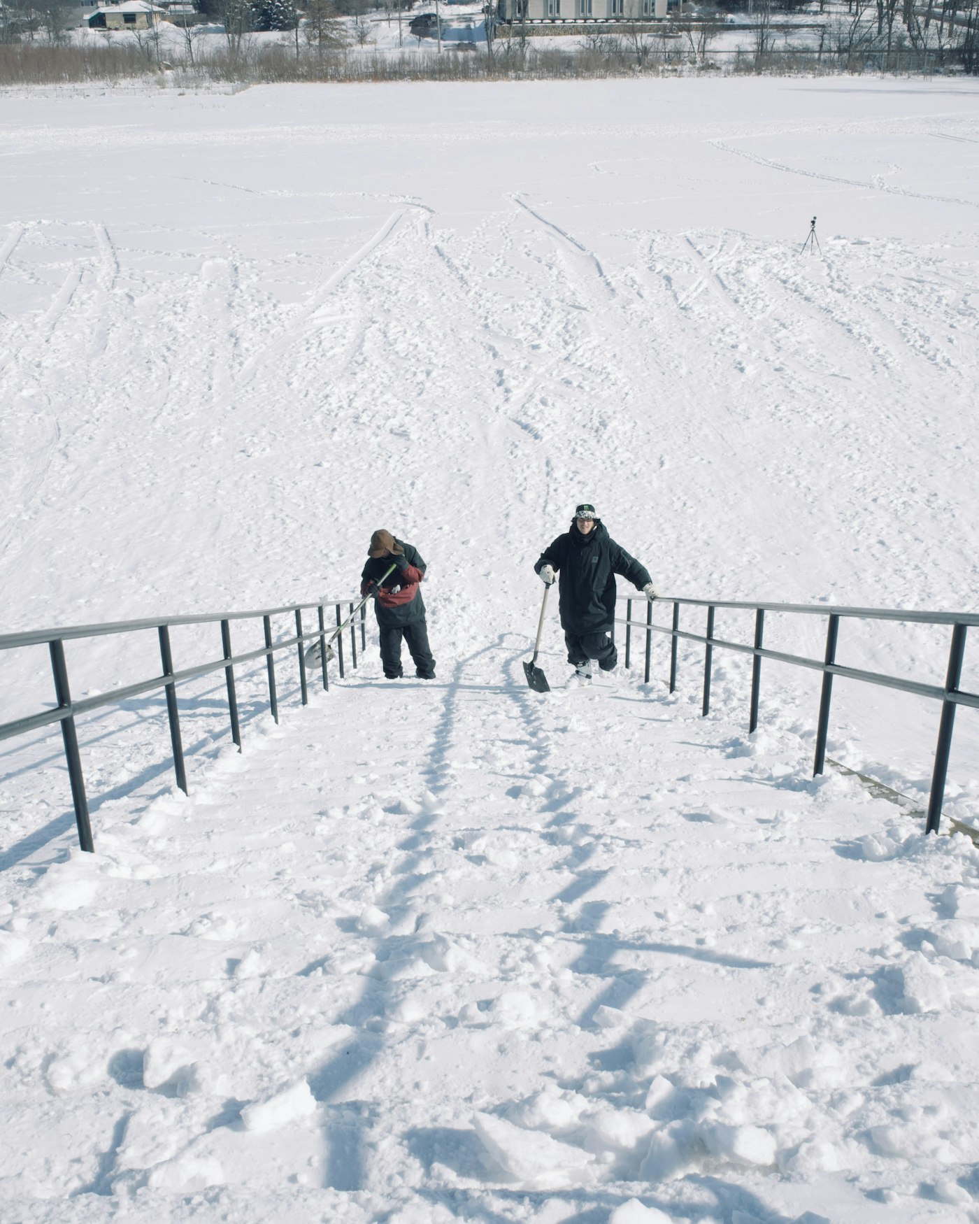 Skiers standing at the bottom of stairs with shovels