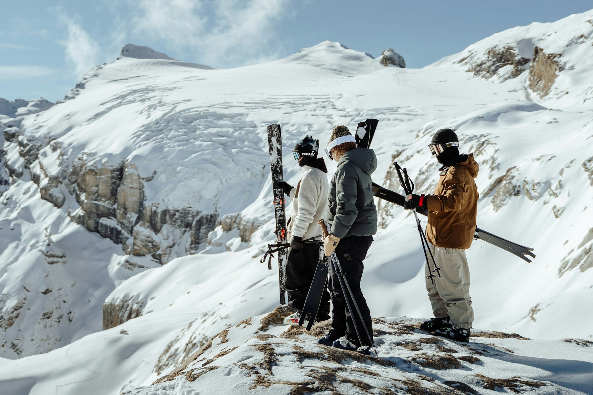 3 skiers look over a snowy ledge onto terrain below