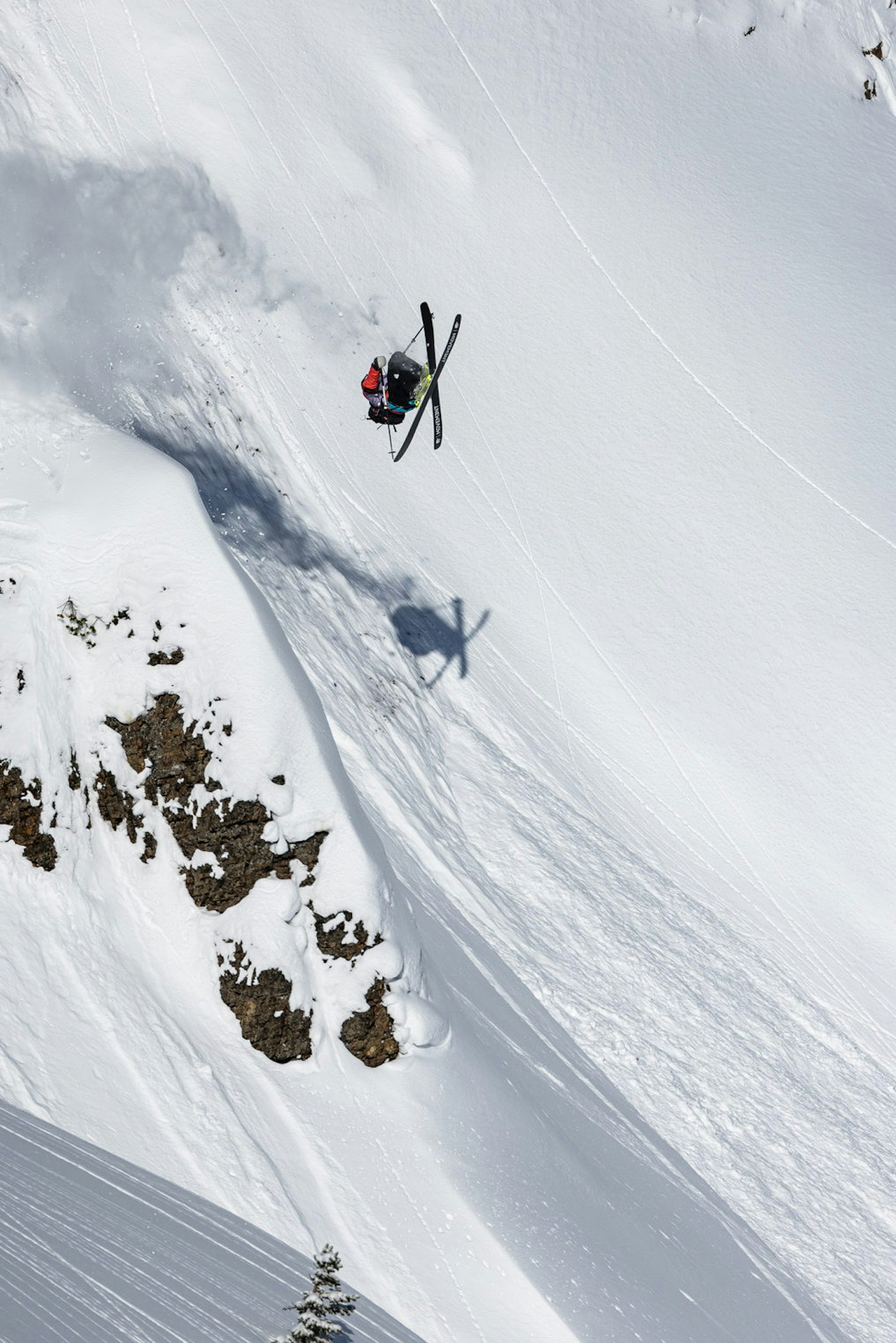 Skier does a backflip with skis crossed off a snowy mountainside