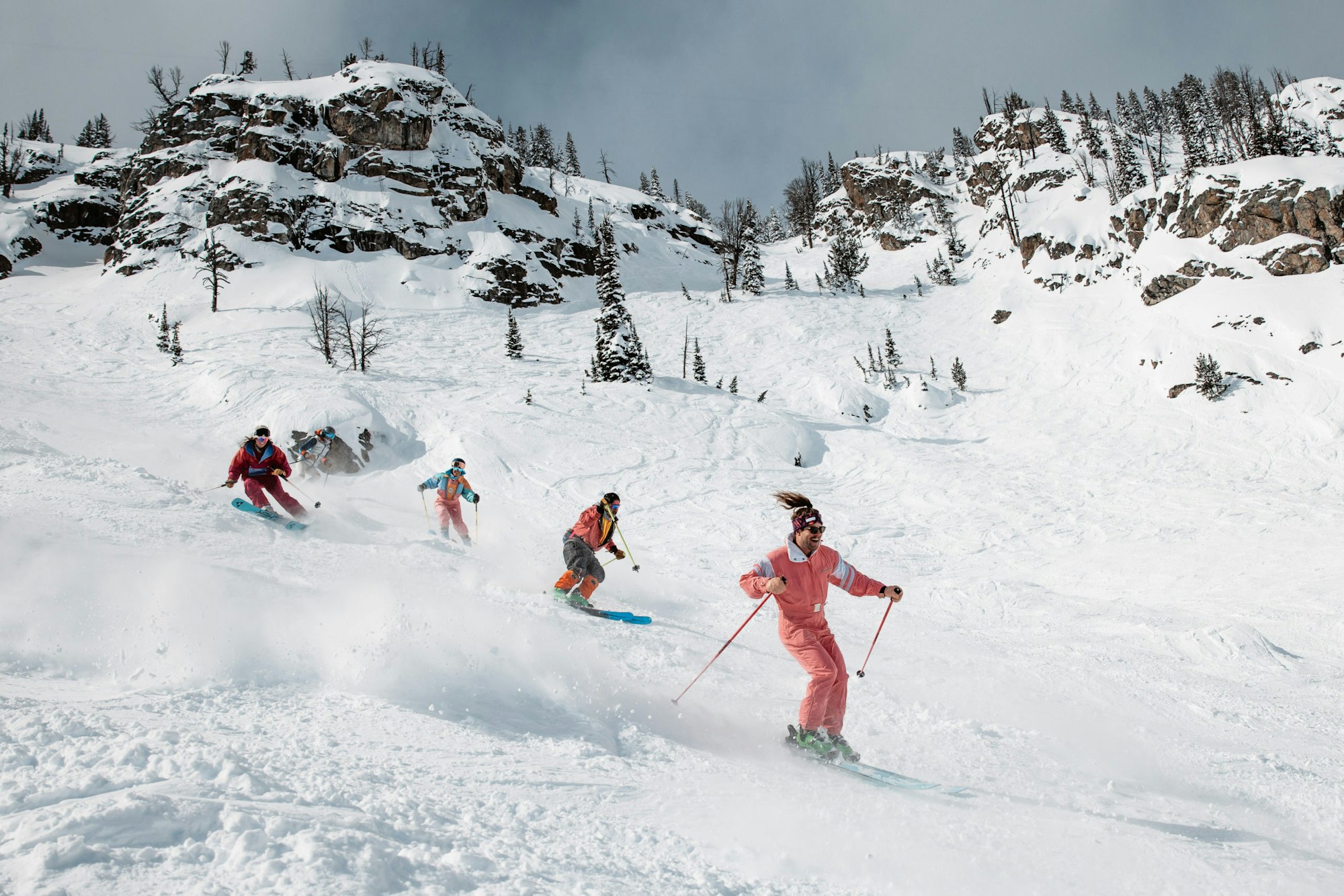 5 skiers skiing in a line down a snowy slope
