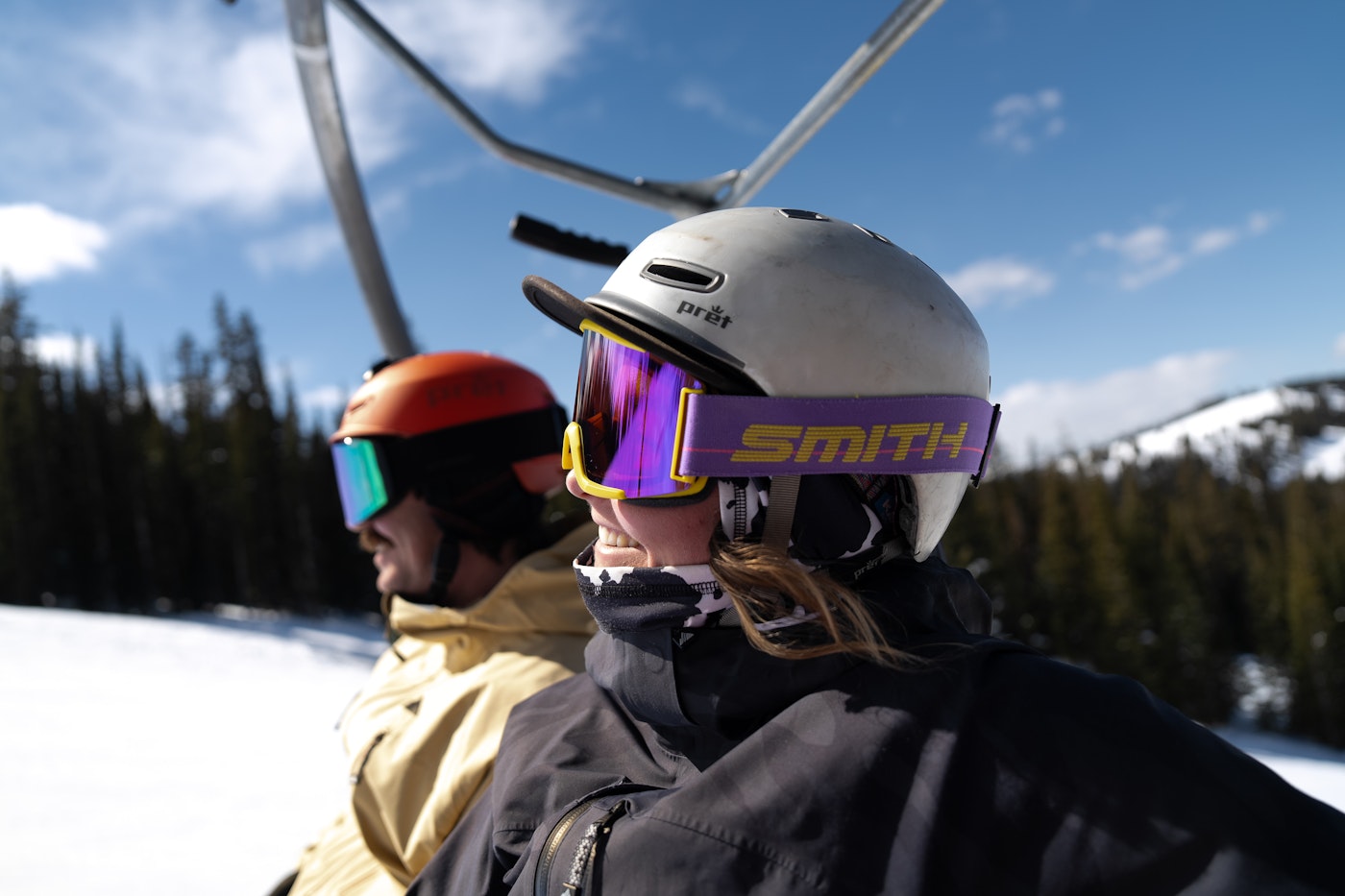 Two skiers wearing goggles on ski lift.