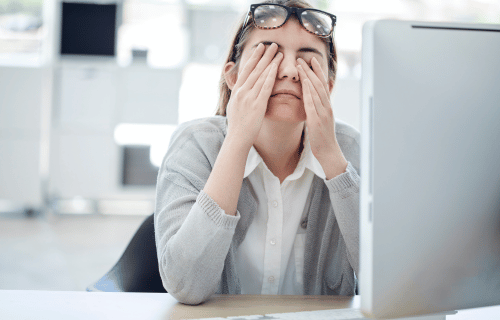 woman rubbing her eyes at her desk